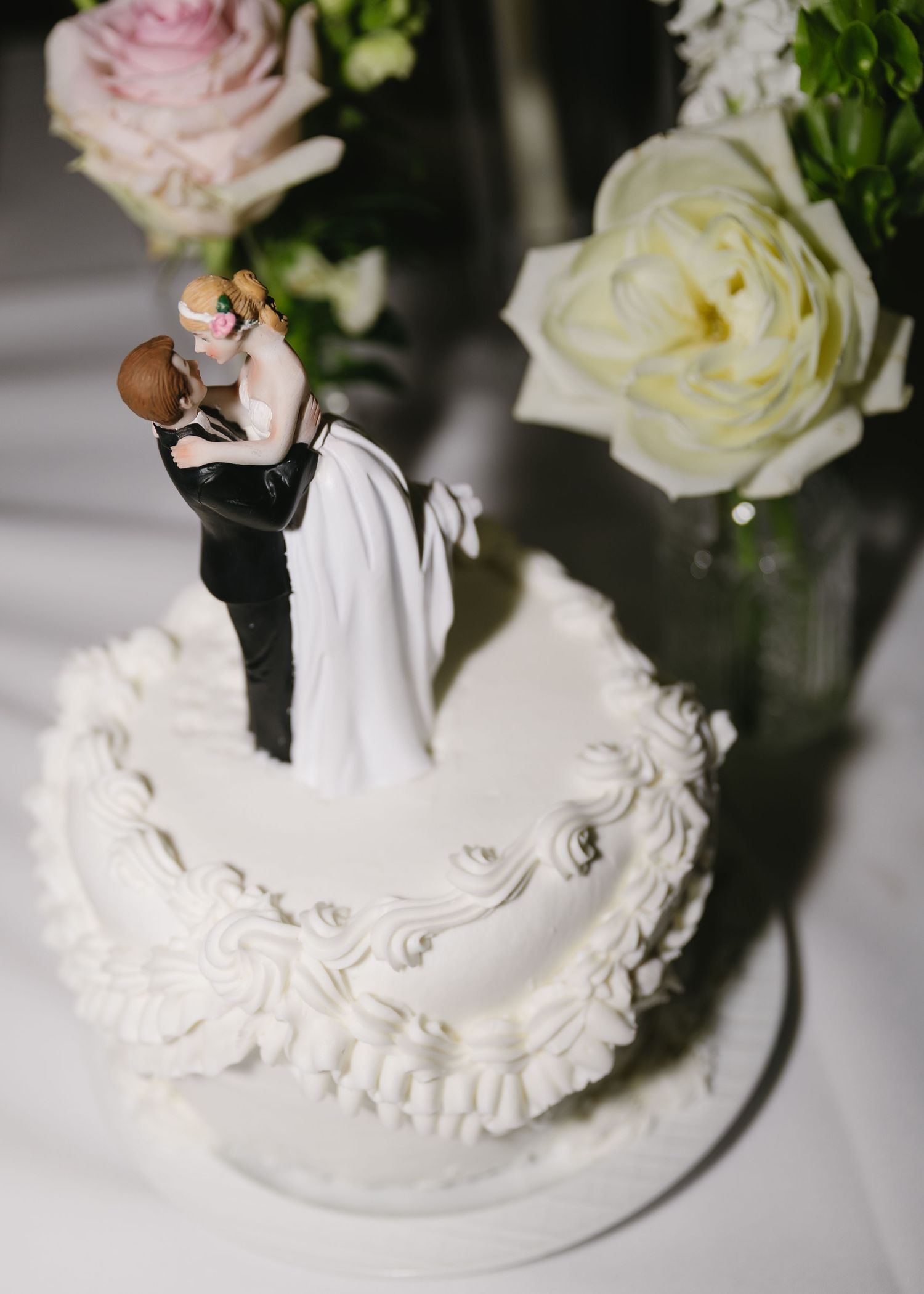 A traditional white wedding cake topper displayed with fresh roses and greenery.
