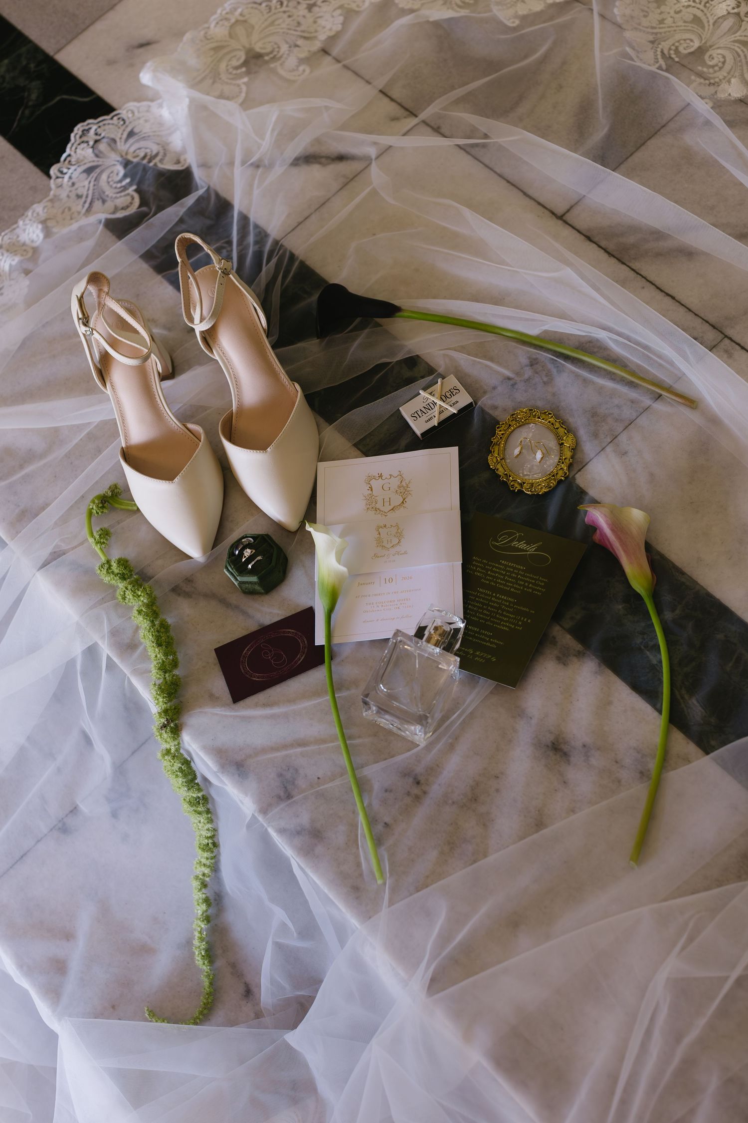 Elegant bridal accessories including white heels and stationery arranged on flowing tulle fabric.
