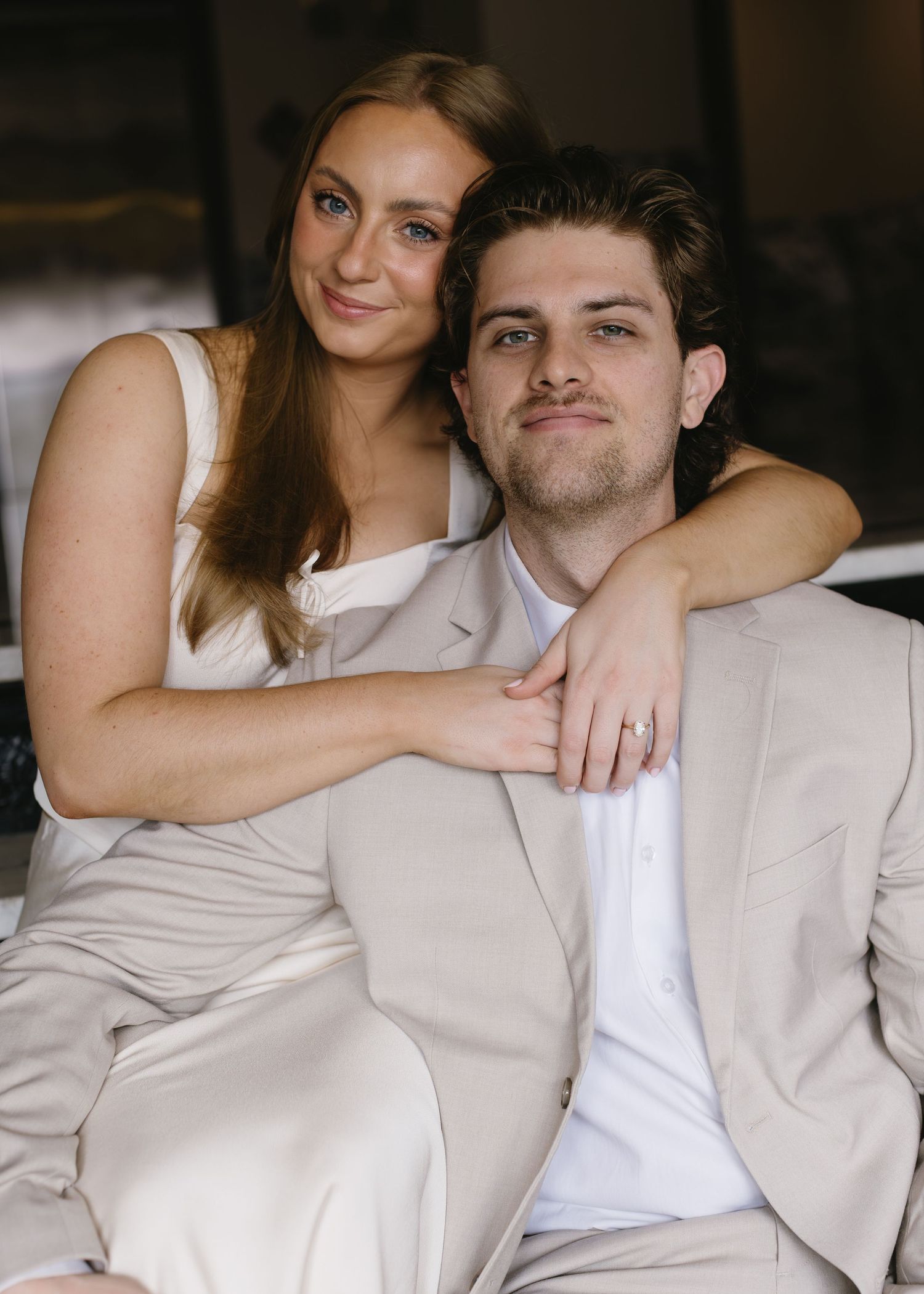 A romantic portrait of a couple in matching cream outfits embracing in an intimate indoor setting.