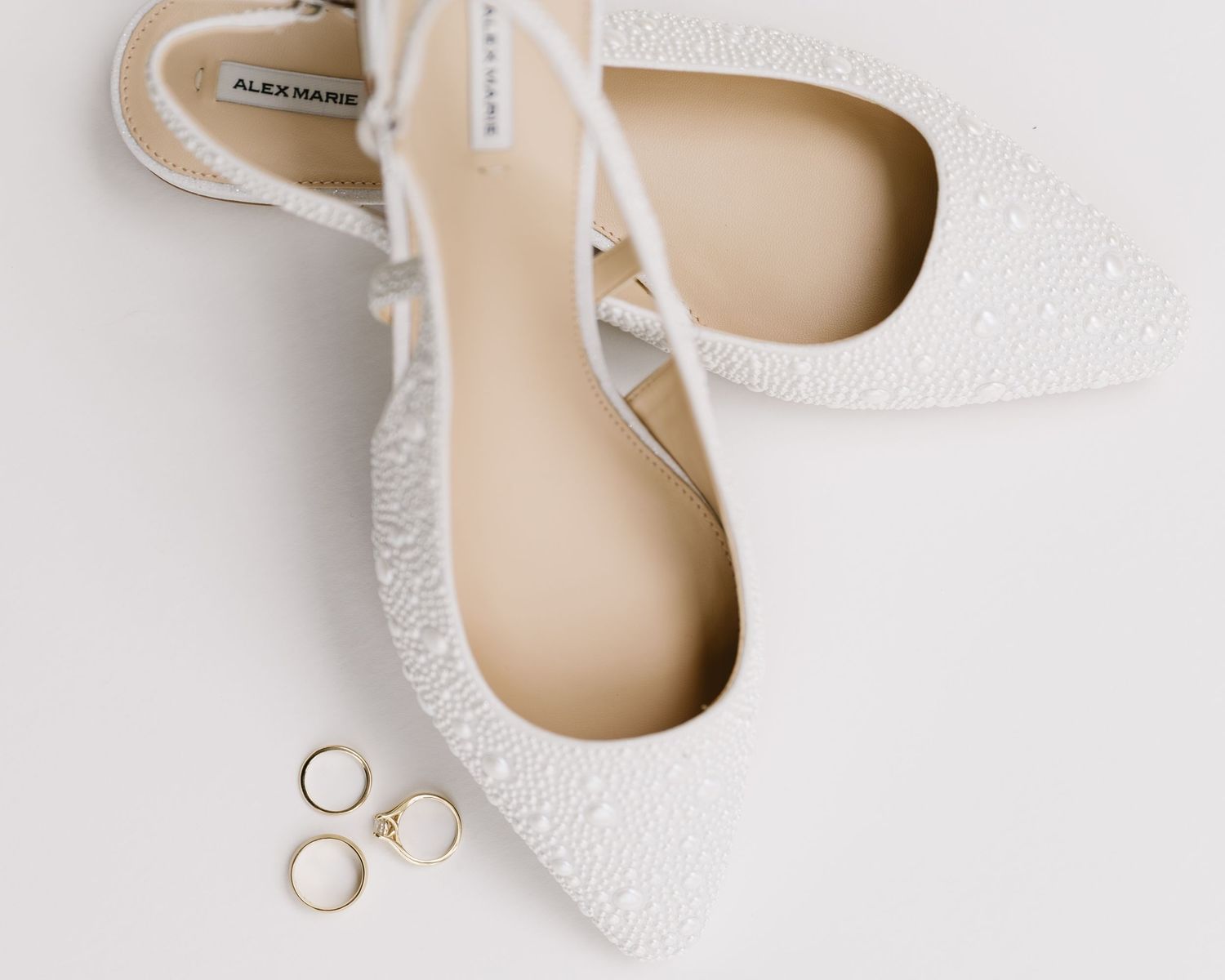 White lace bridal flats with wedding rings on light background.