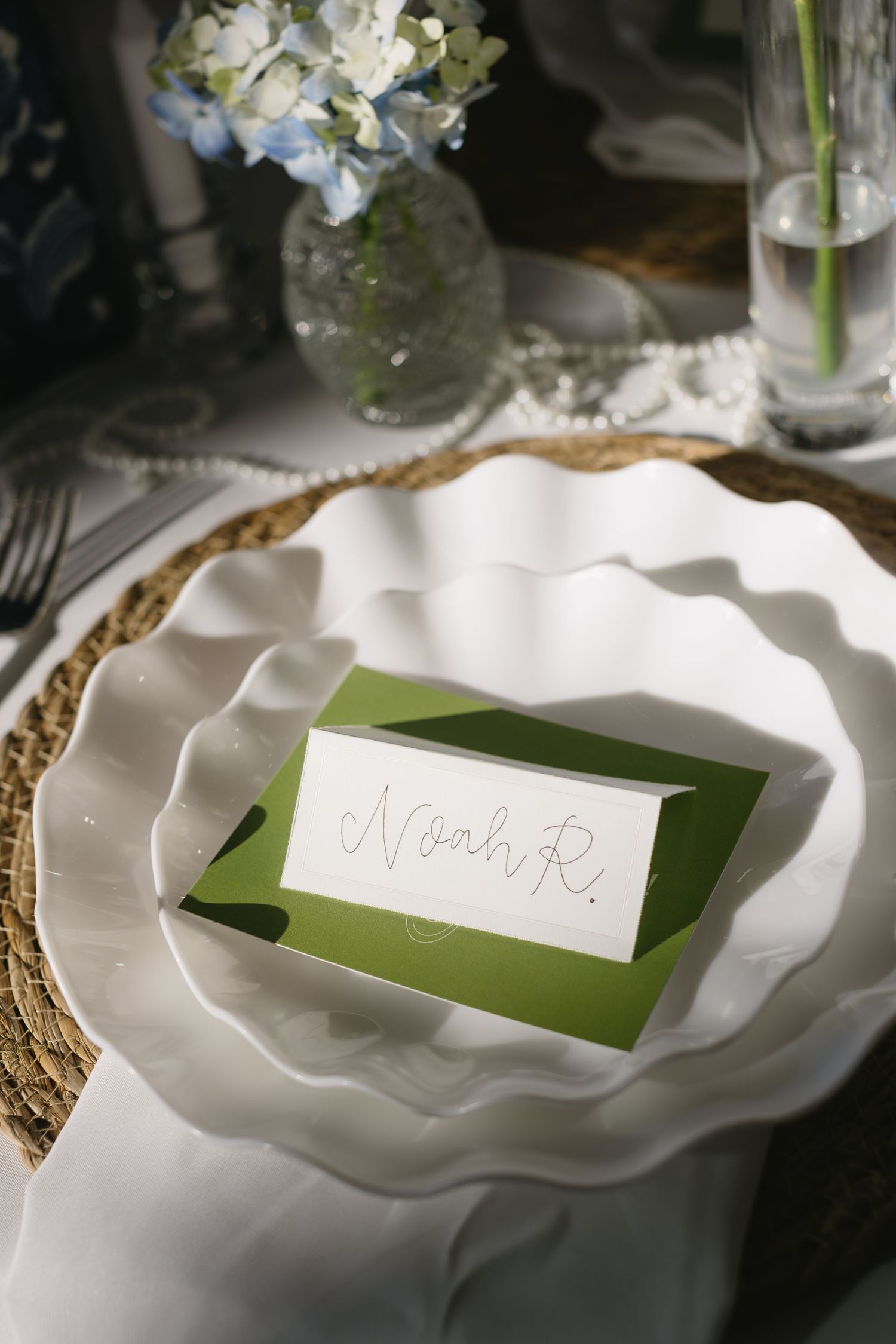 Elegant wedding place setting with white scalloped plates and green name card on gold charger.