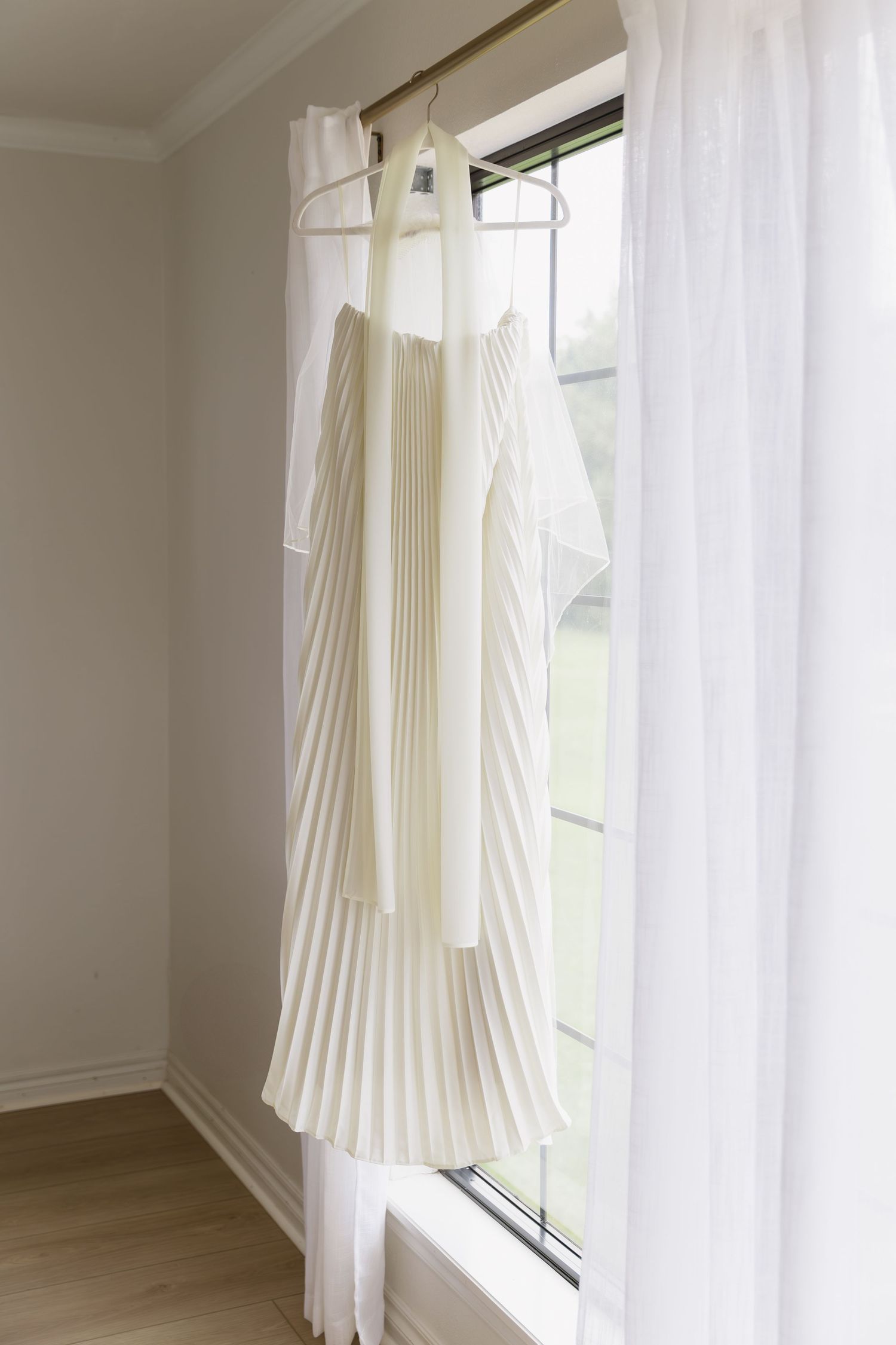 White pleated curtain panel hangs elegantly beside a window, creating soft filtered light in a modern room interior.