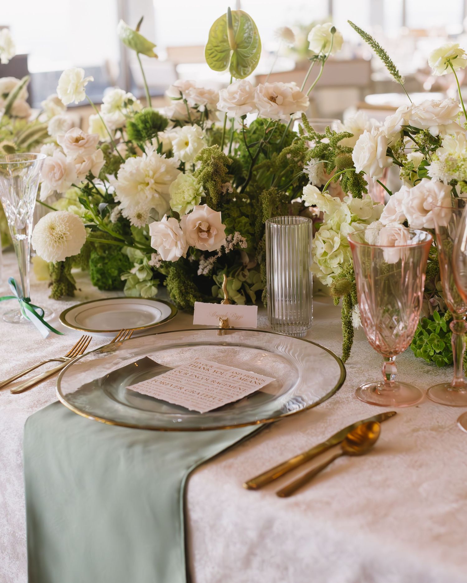 Romantic wedding table setting with soft pink flowers and sage green accents.