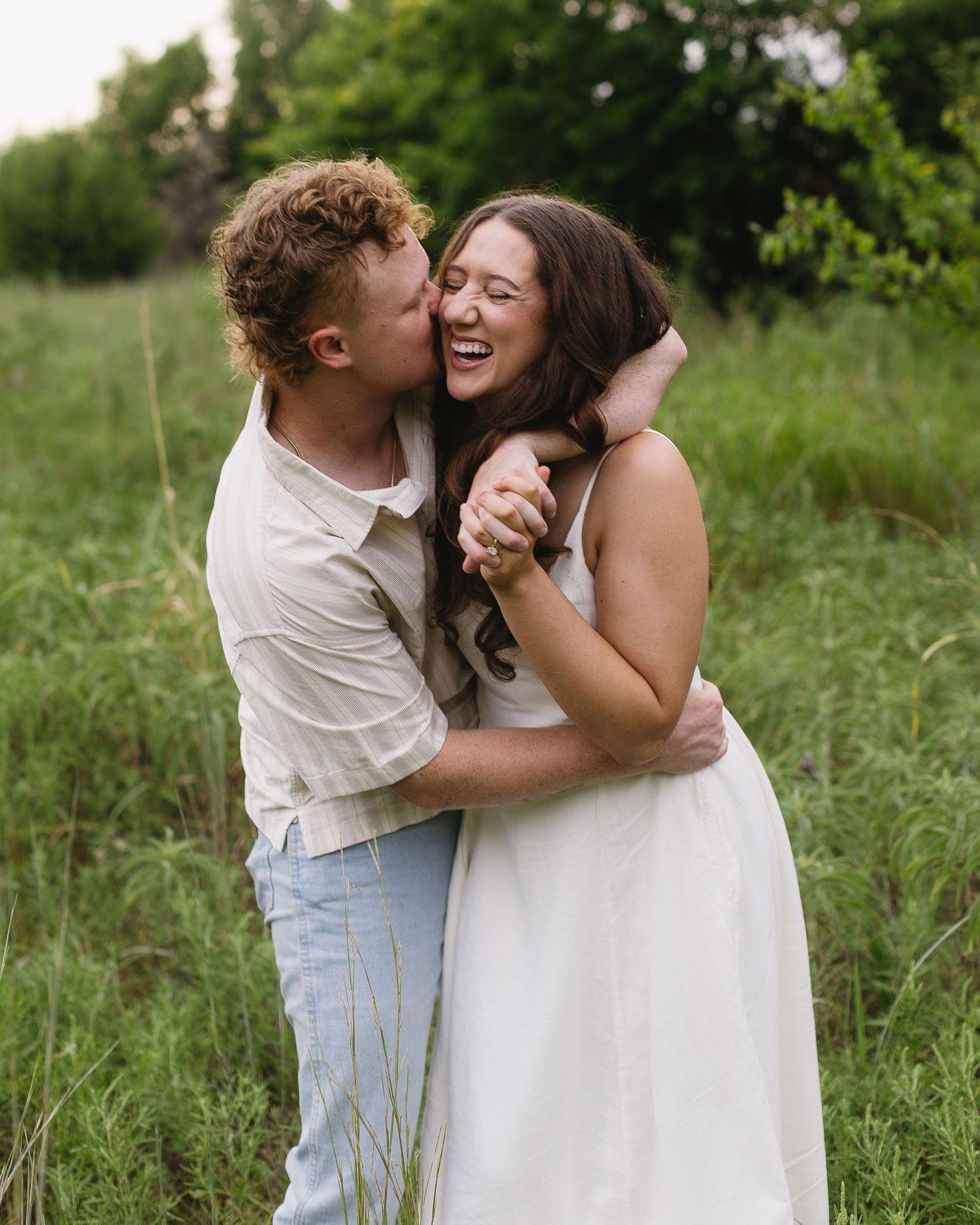A joyful couple embraces and laughs together in a green summer meadow filled with tall grass.