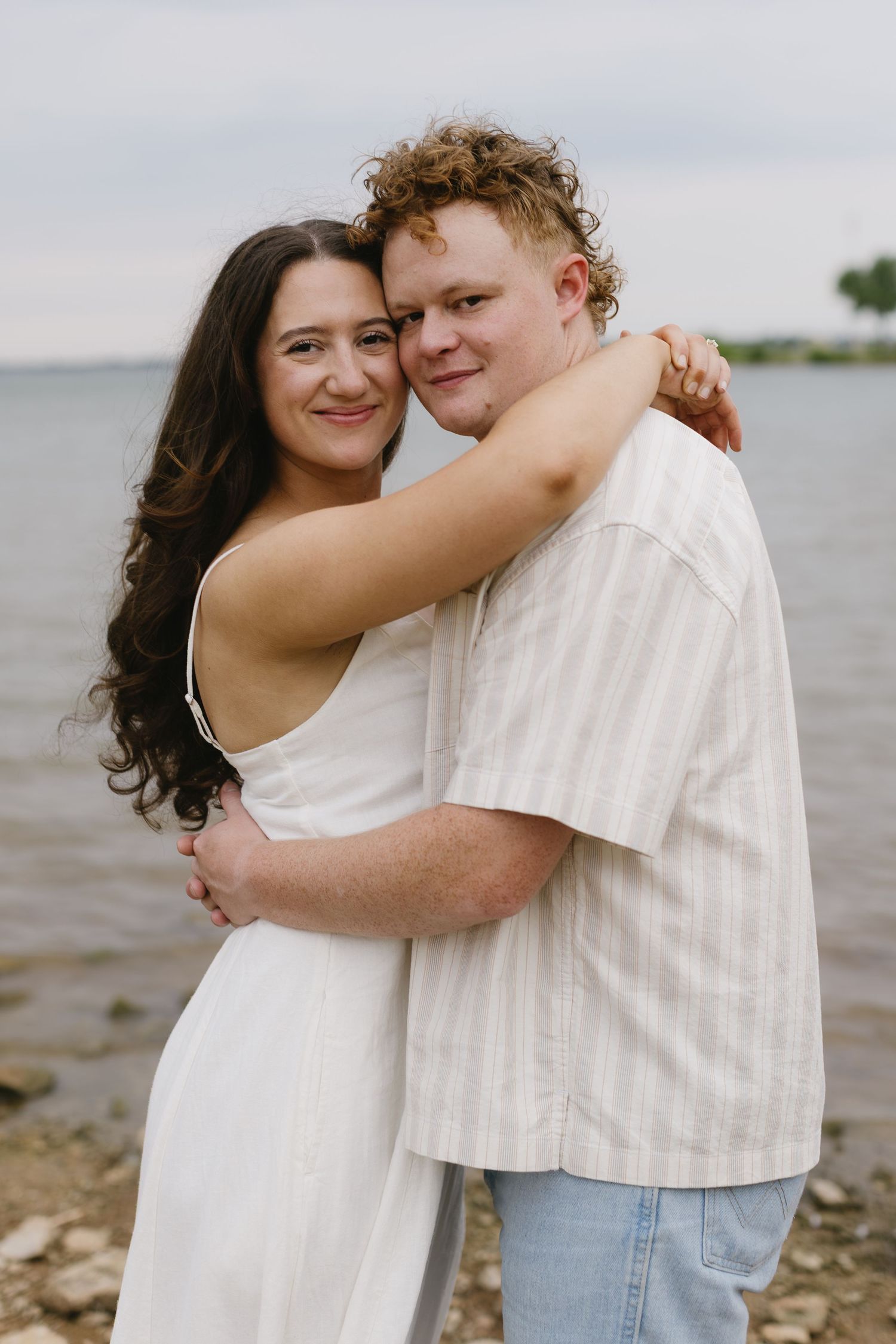 Young couple in white and denim embracing and sharing joyful moments near a lake.