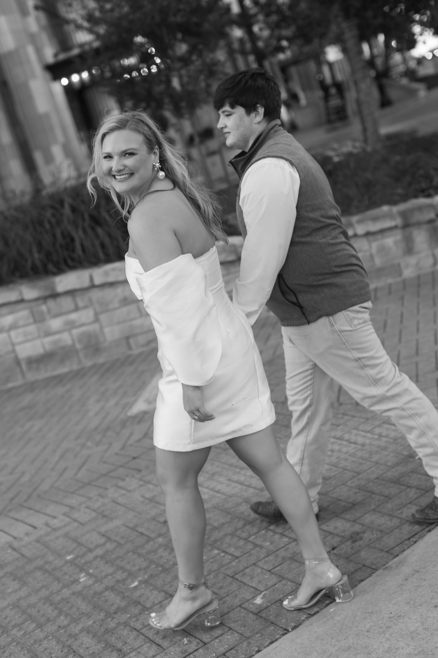A playful moment captured in black and white of a couple dancing together on a brick paved walkway.