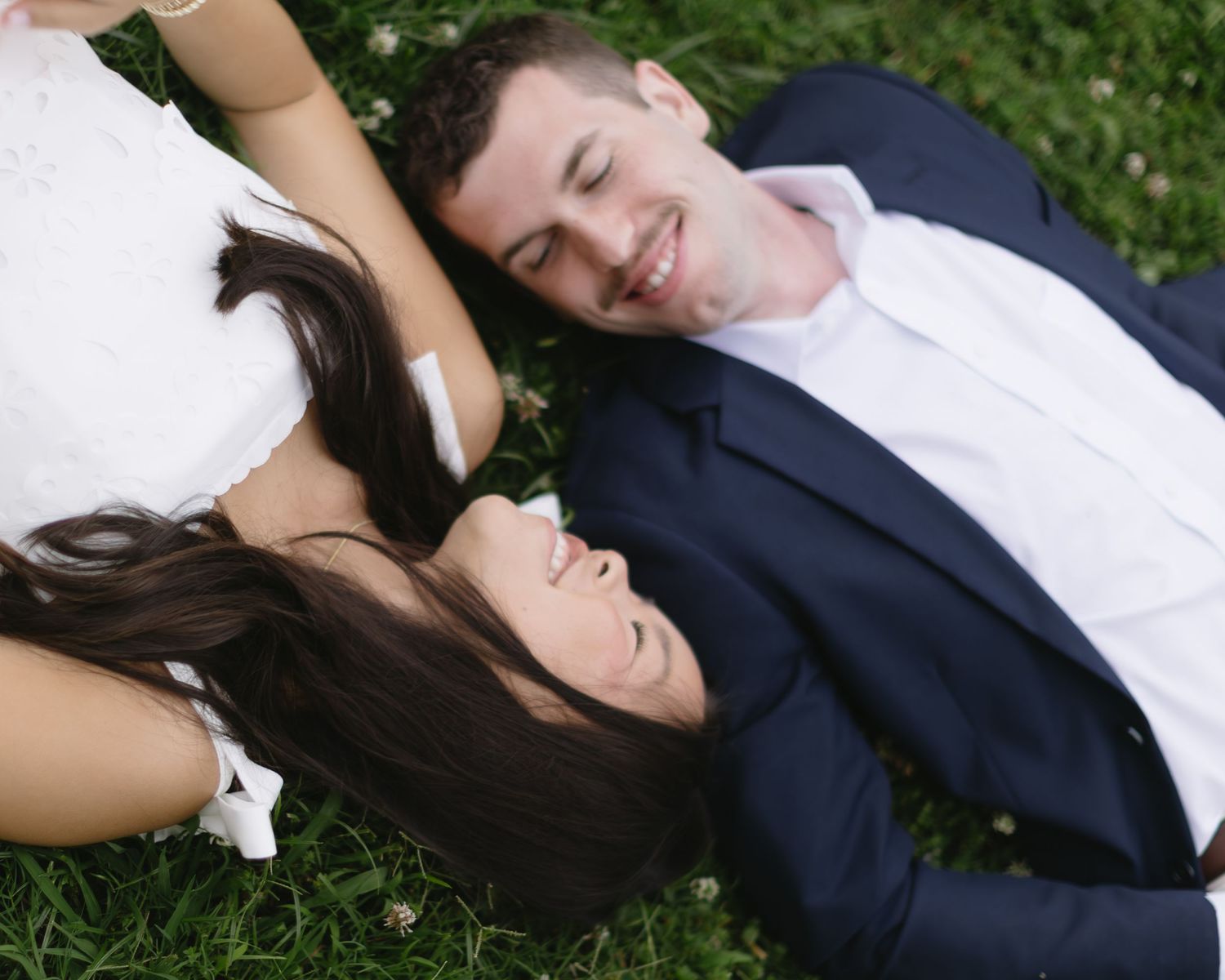 A couple lies on their sides in the grass during a romantic outdoor photo session.