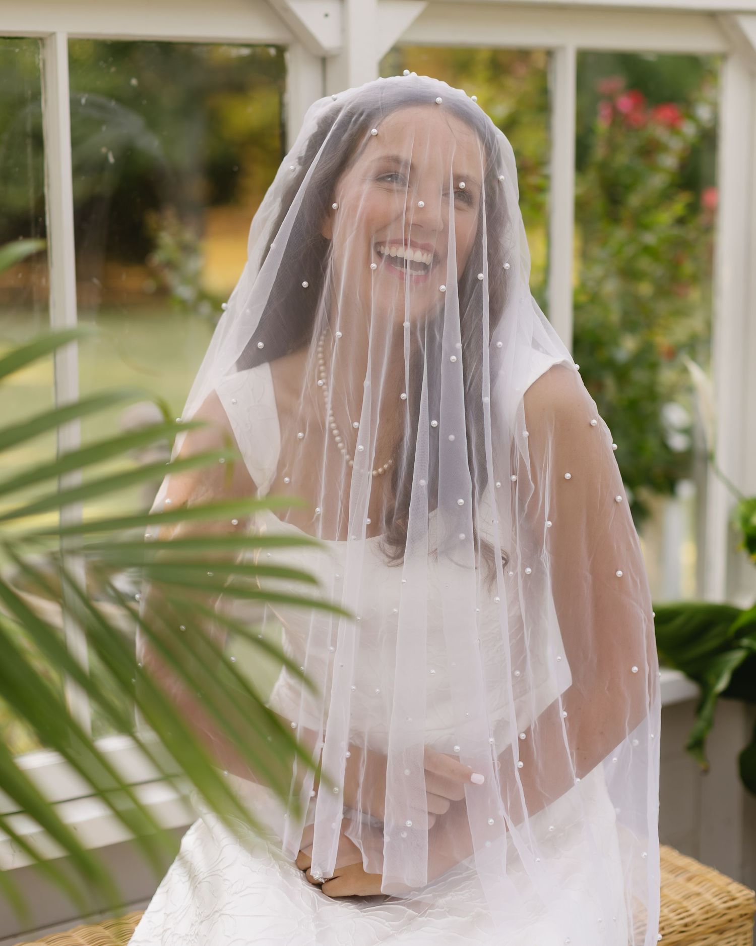A joyful moment captured through a crystal-embellished bridal veil in a garden gazebo setting.