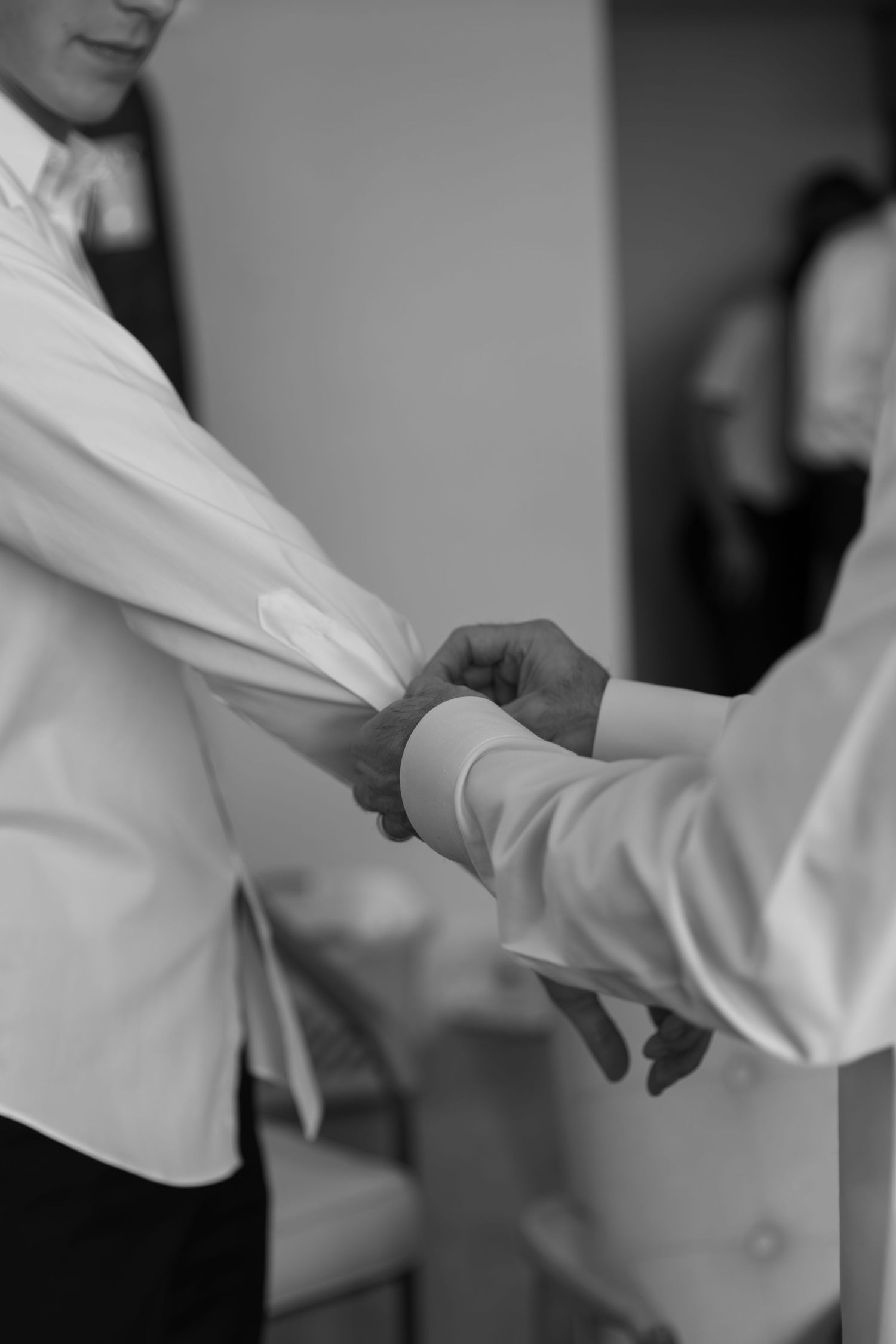 Close-up of hands adjusting white formal attire sleeves in black and white.