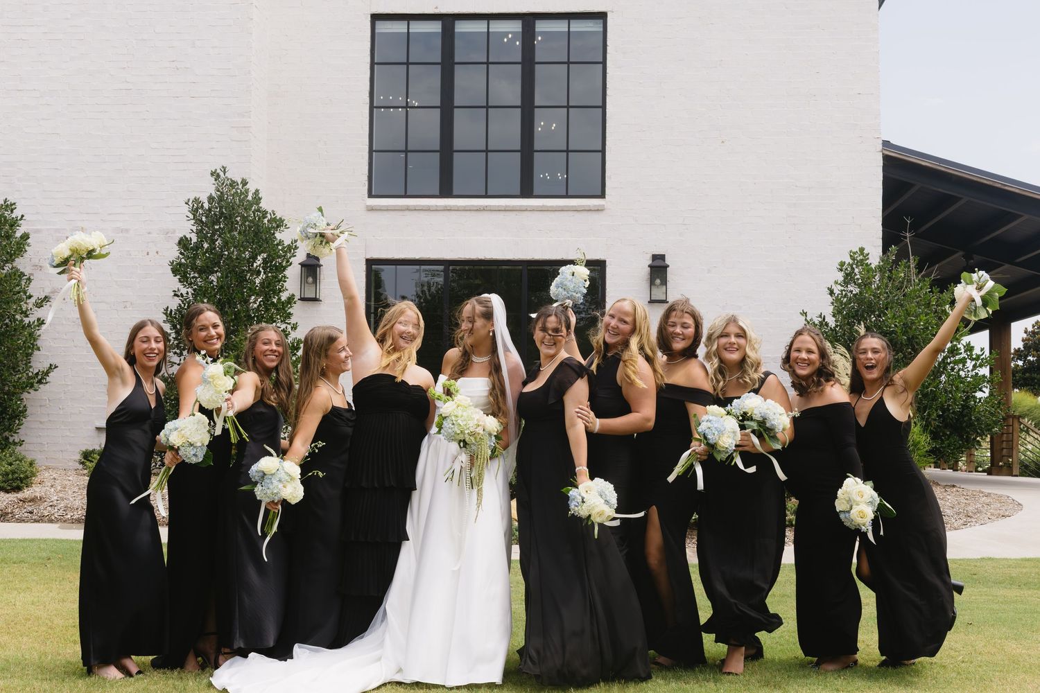 Wedding party in black and white dresses celebrating outdoors with raised arms.