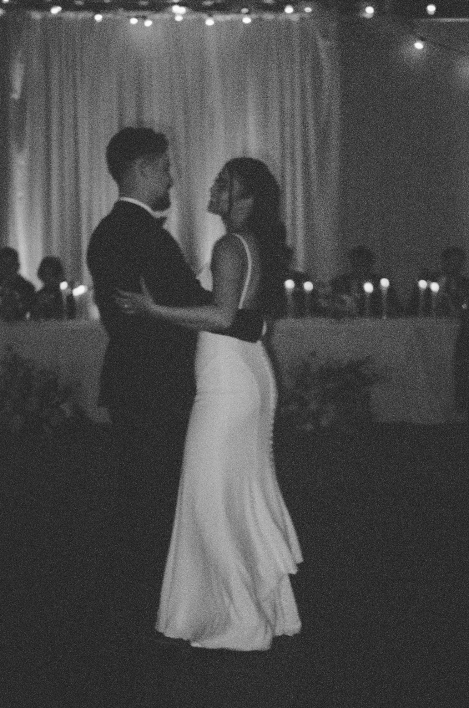 A couple shares a romantic dance under twinkling lights at their wedding reception.