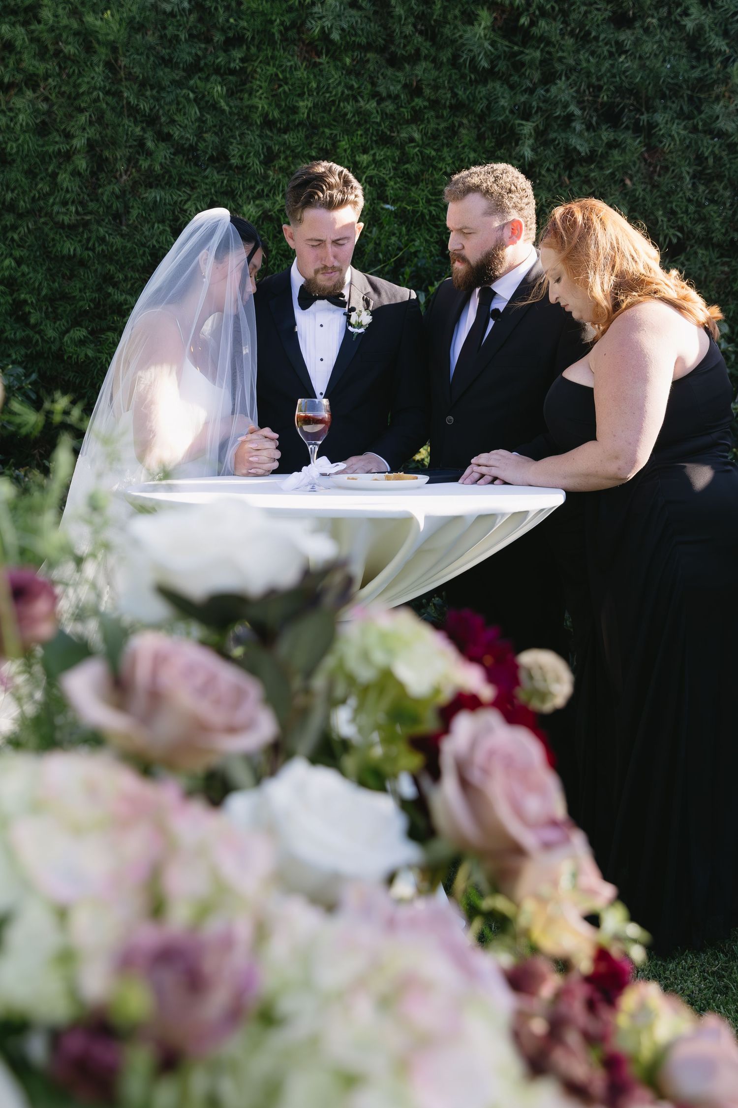 Wedding ceremony details with pink and white flowers in the foreground and guests in formal attire.