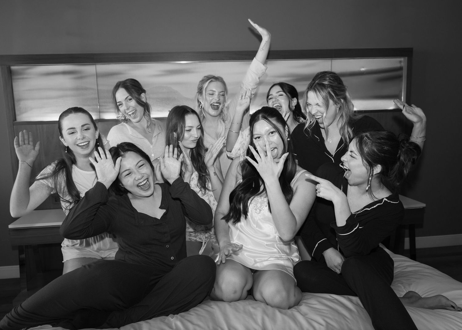 A candid black and white photo of wedding guests laughing and celebrating together on a bed.