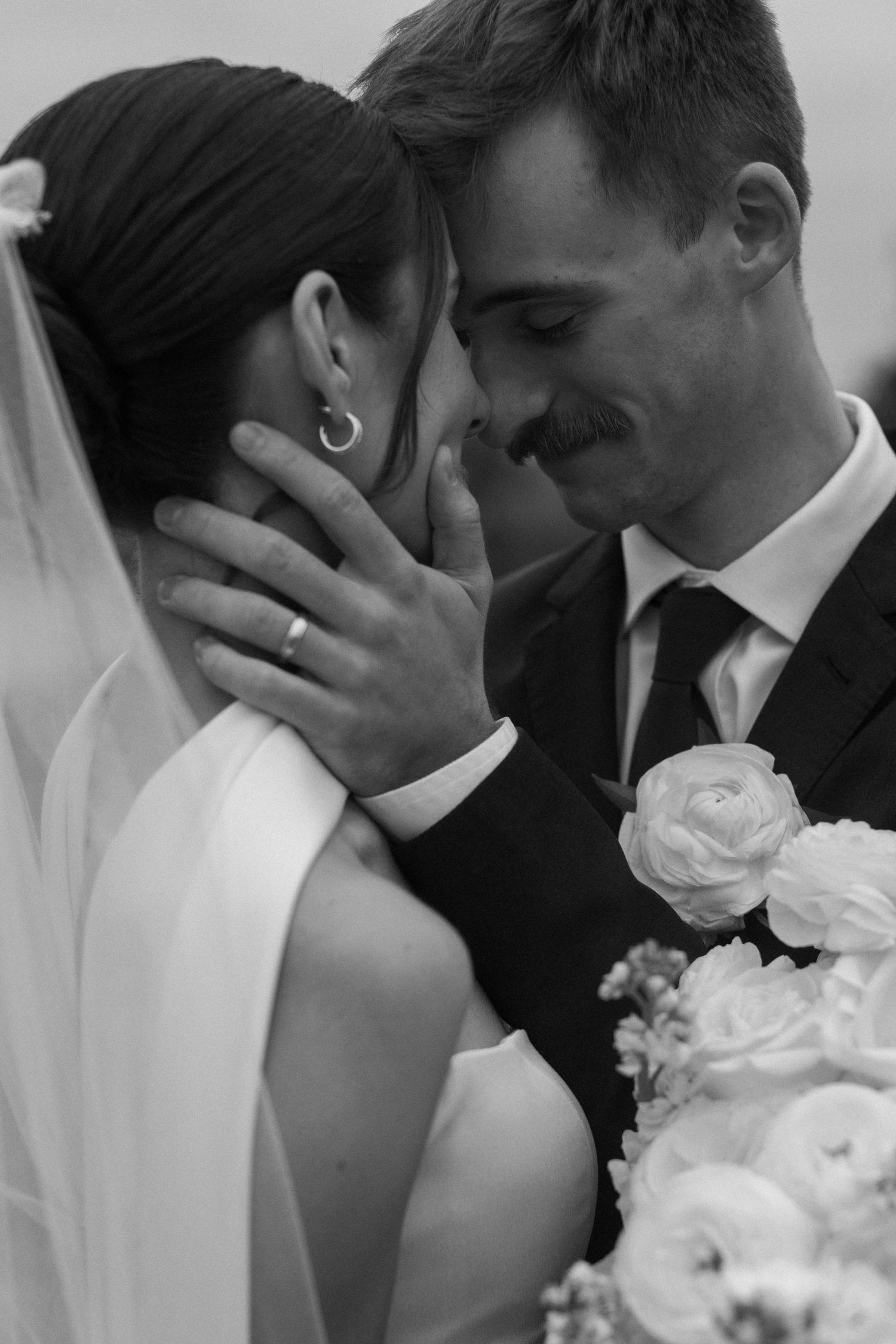 A romantic black and white wedding photo sequence showing a tender kiss between newlyweds with white flowers.