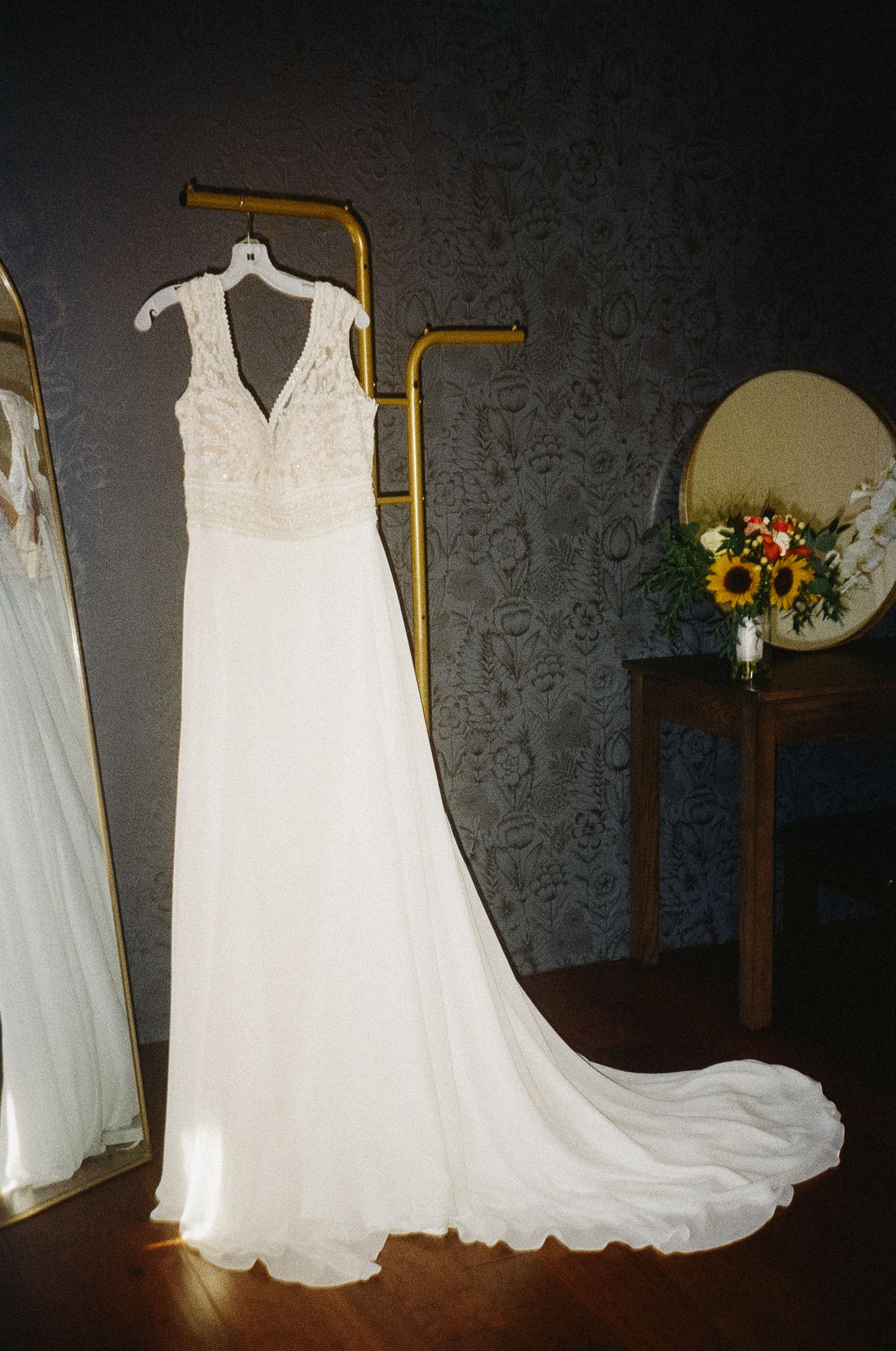 Multiple elegant white wedding dresses displayed on hangers against a dark wall with decorative wallpaper.
