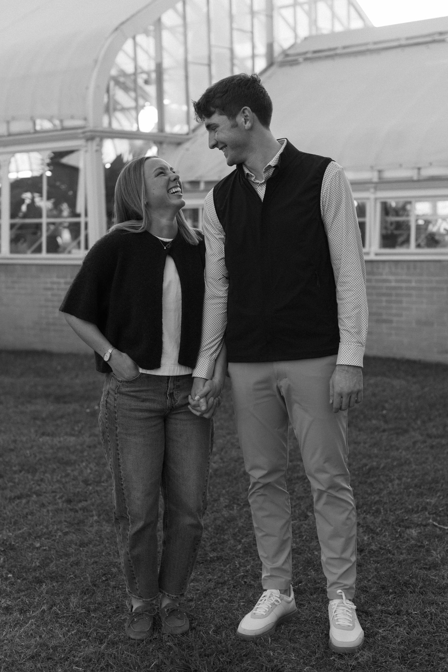 A couple laughing and walking together outdoors in casual attire on a sunny day.