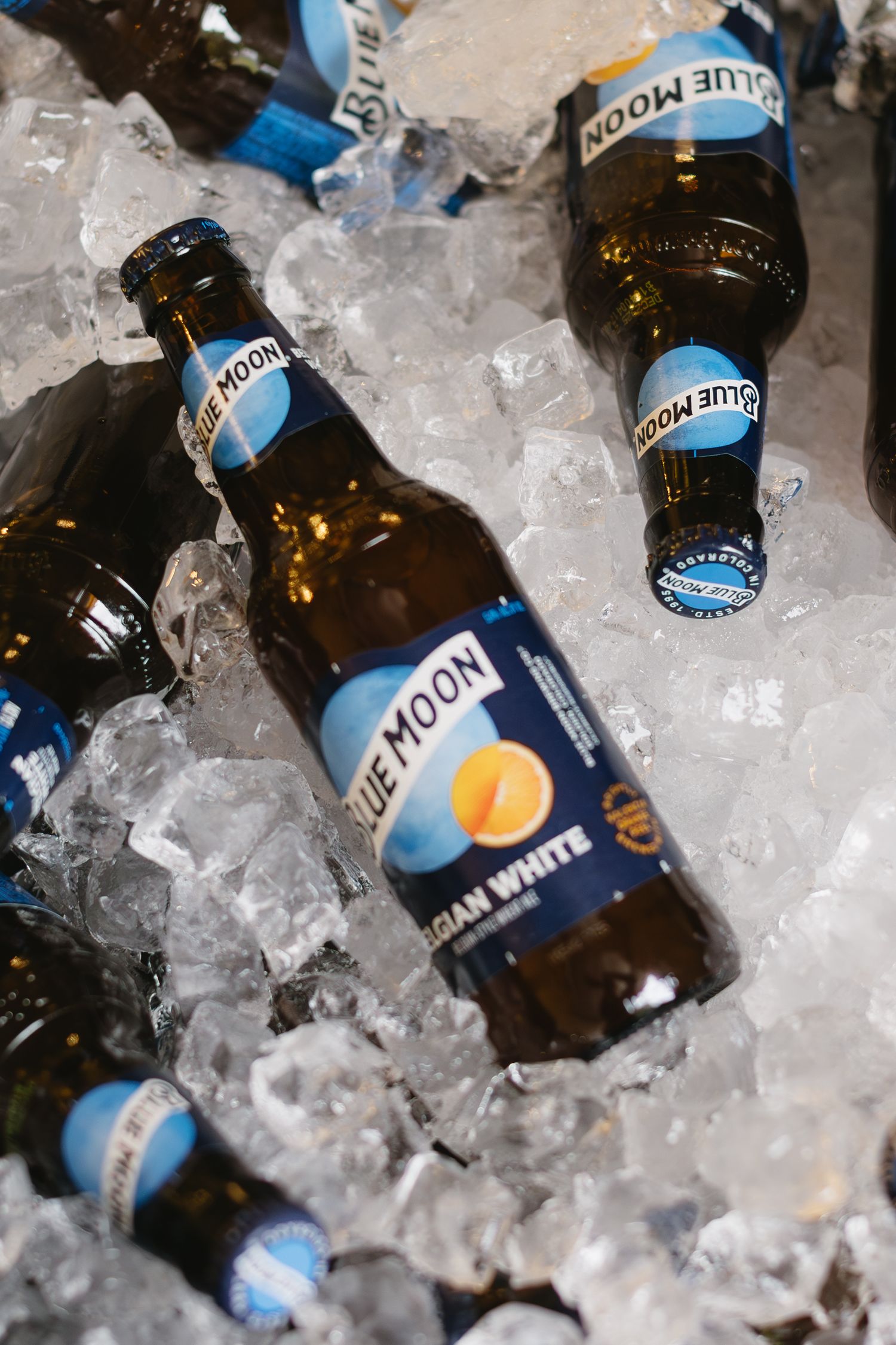 Blue Moon beer bottles nestled in crushed ice create a refreshing display at a bar or party setting.