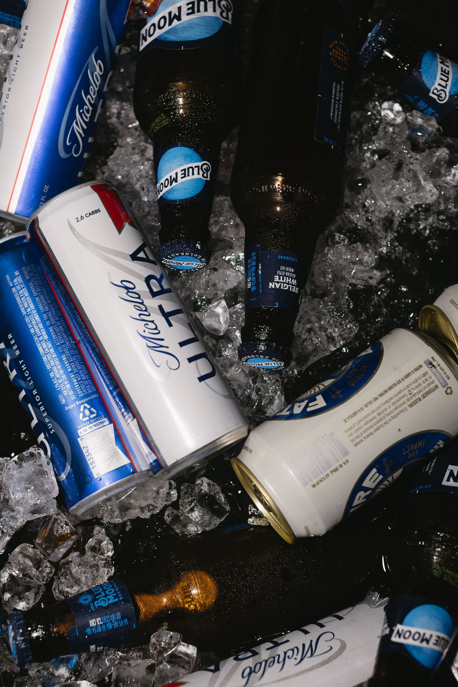 Blue and white beer cans and bottles chilling in ice at a party.