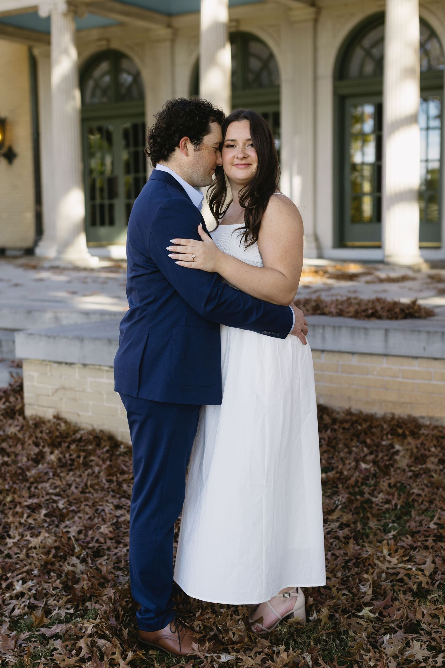 A couple shares intimate moments in a series of photos taken under a covered walkway with white columns.