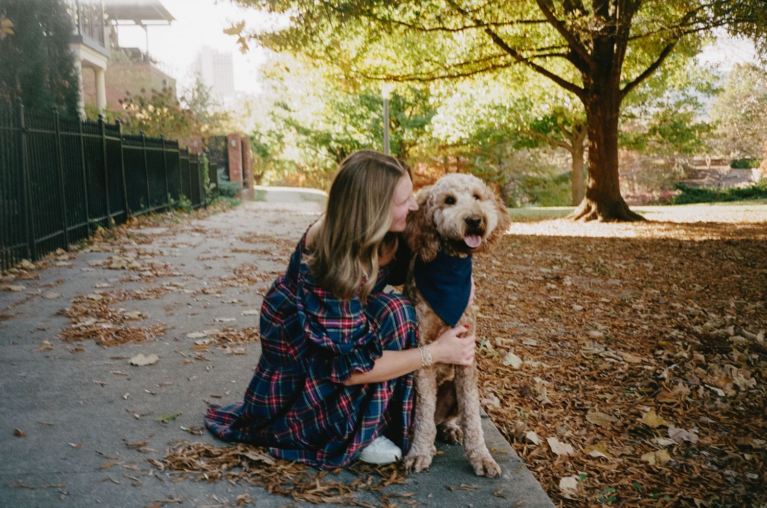 Two people sit together with a golden retriever dog on fallen autumn leaves in a park setting.