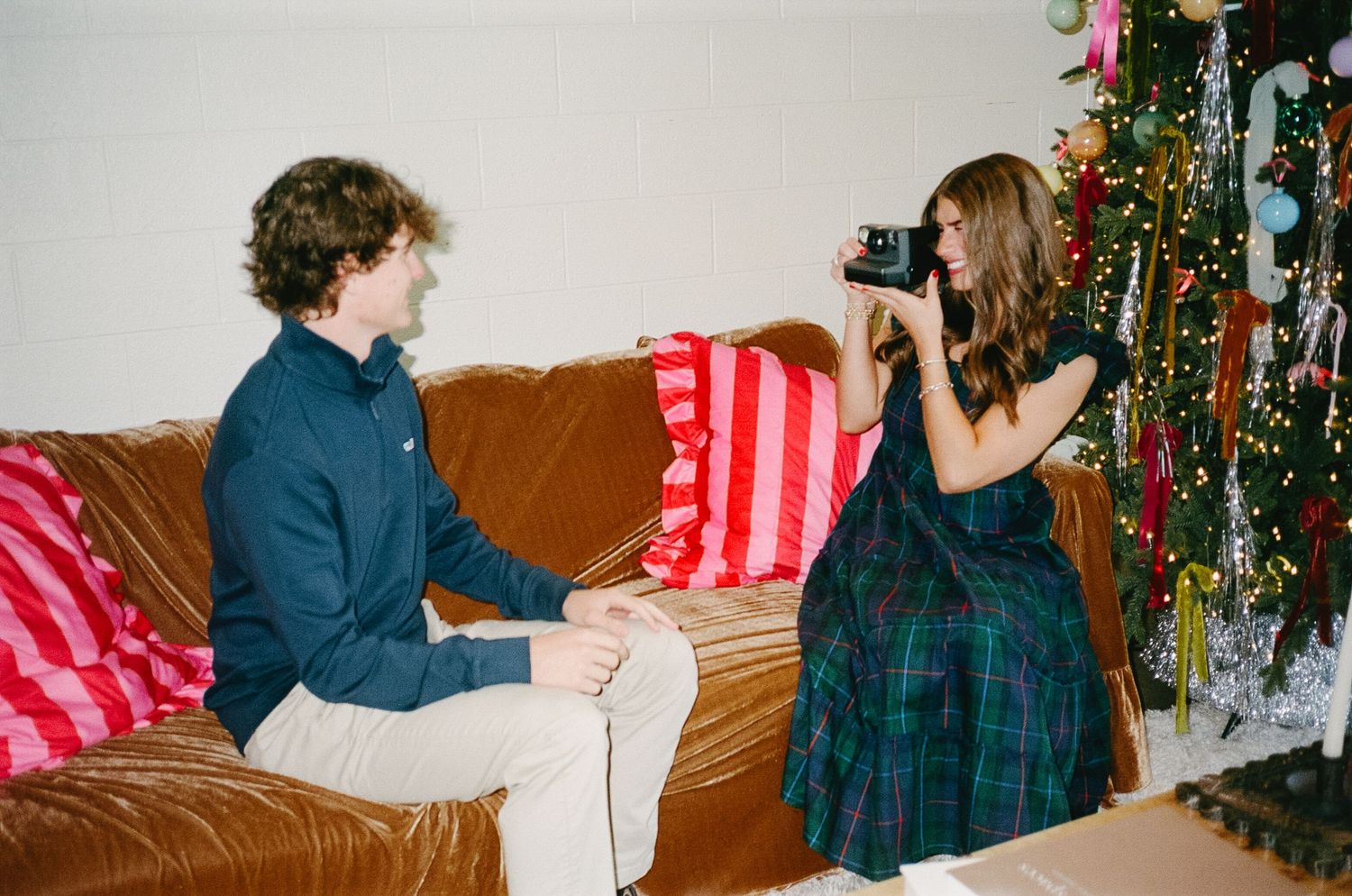 Someone takes a photo with a camera while sitting on a brown leather couch next to a decorated Christmas tree.