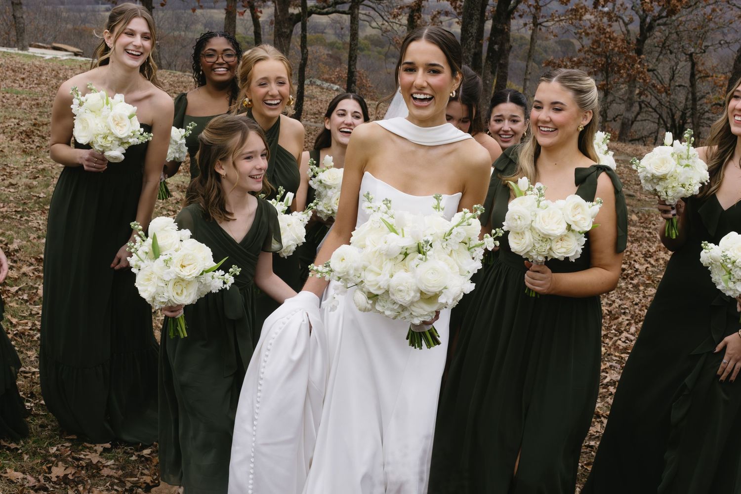 Bridal party laughing together outdoors while holding white floral bouquets.