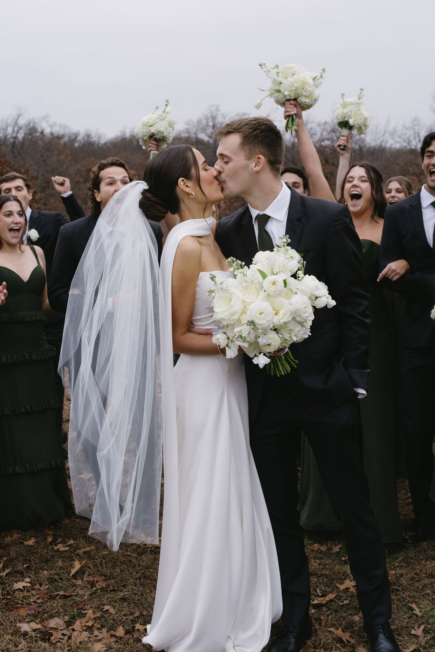 Wedding party celebrates outdoors with white floral bouquets against an autumn backdrop.