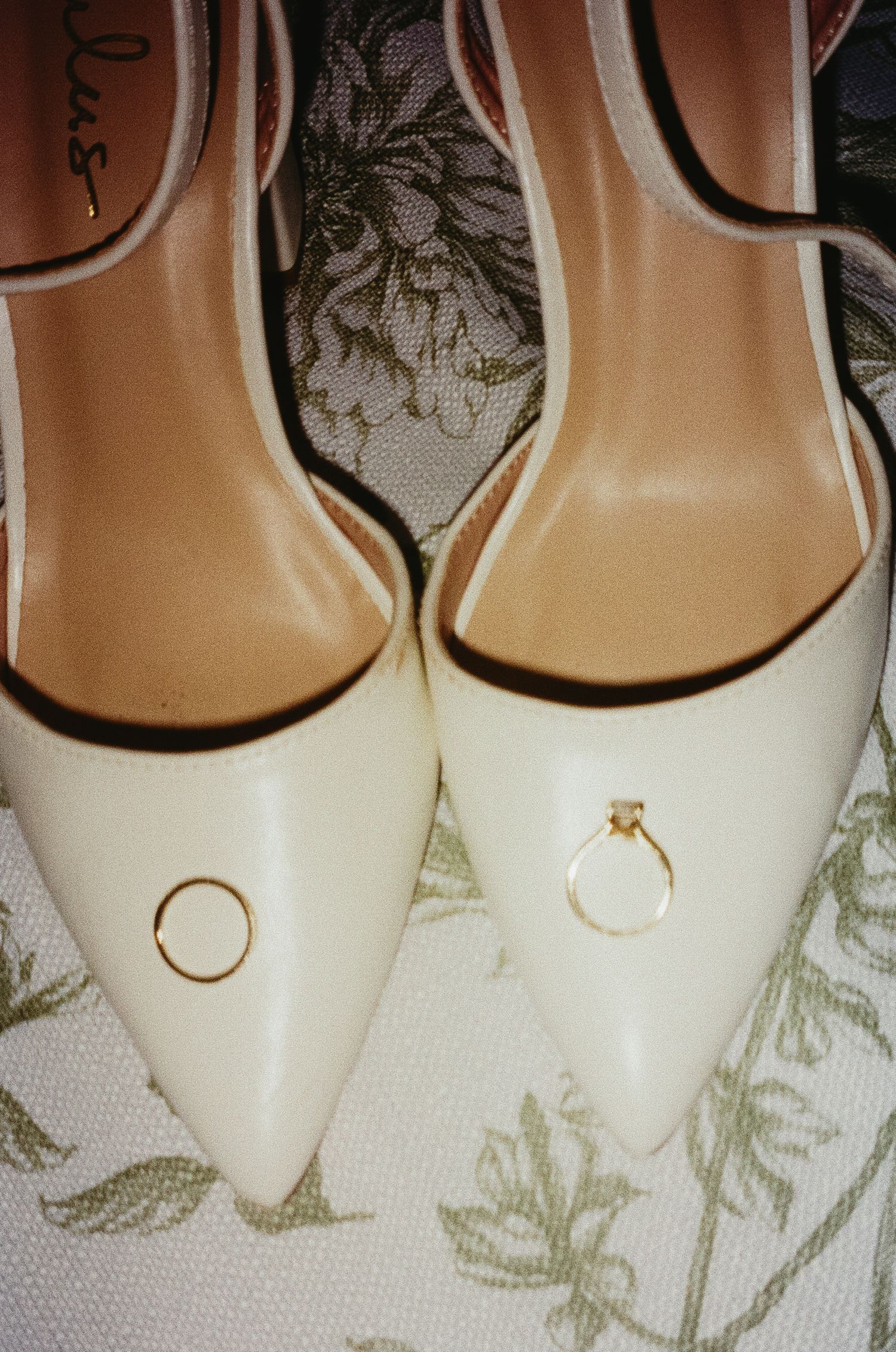 White bridal shoes arranged in a row with wedding rings balanced on their toes.