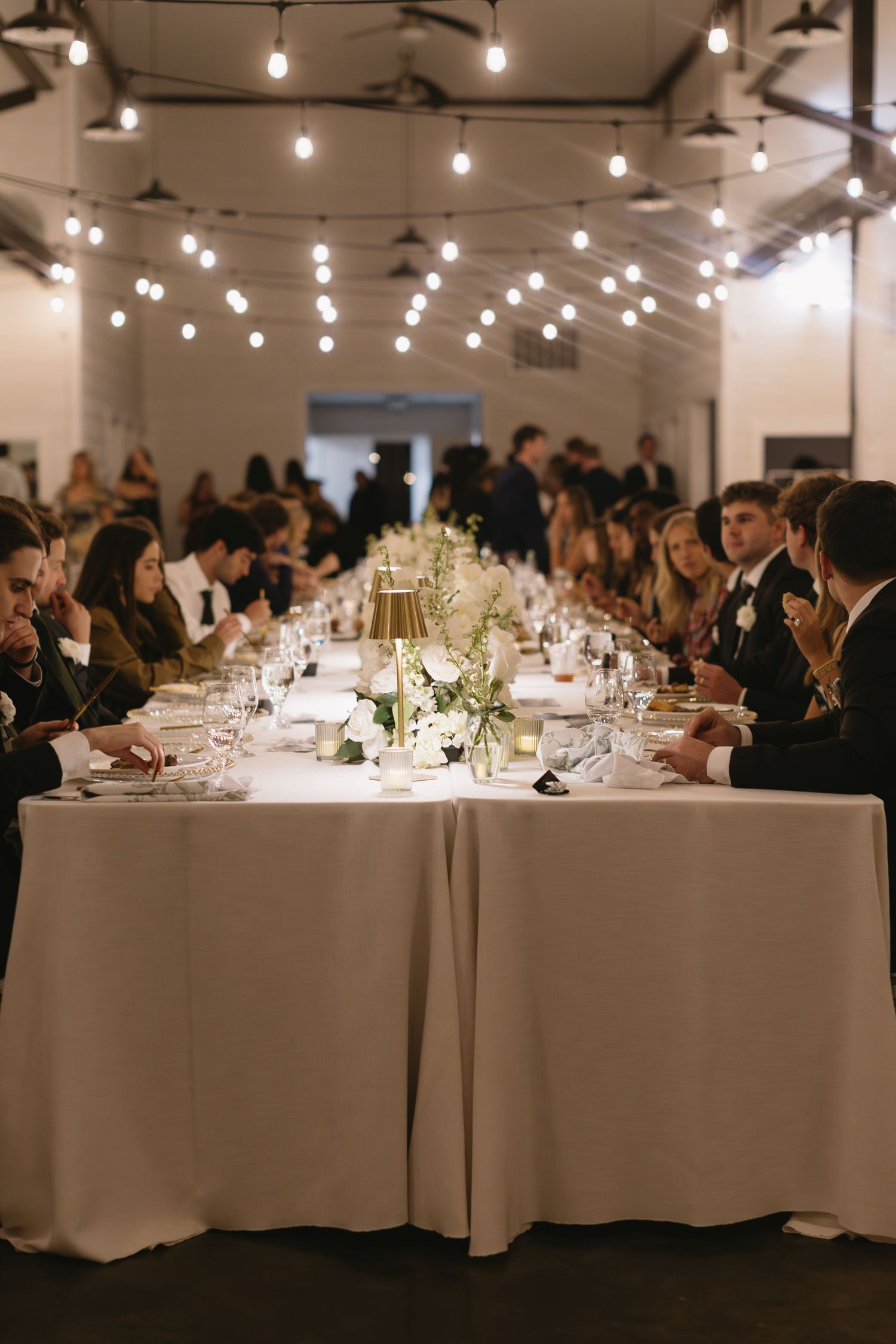 Elegant wedding reception dinner setup with string lights and long tables.