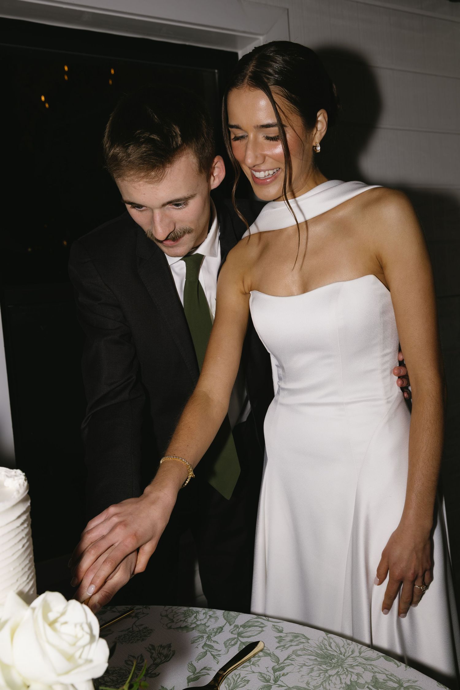 A joyful moment shared while cutting the elegant white wedding cake.