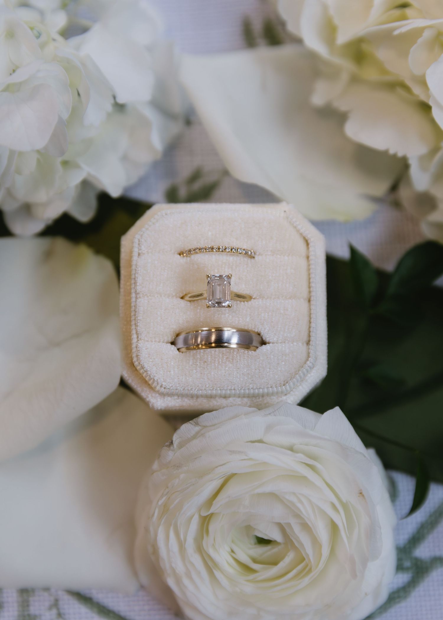 Wedding rings nestled in cream velvet boxes displayed alongside white roses and delicate floral arrangements.