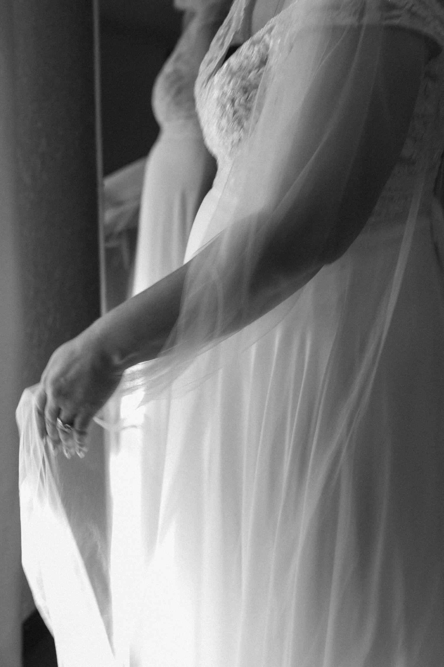 Artistic black and white detail shot of wedding dress lace and flowing veil fabric.