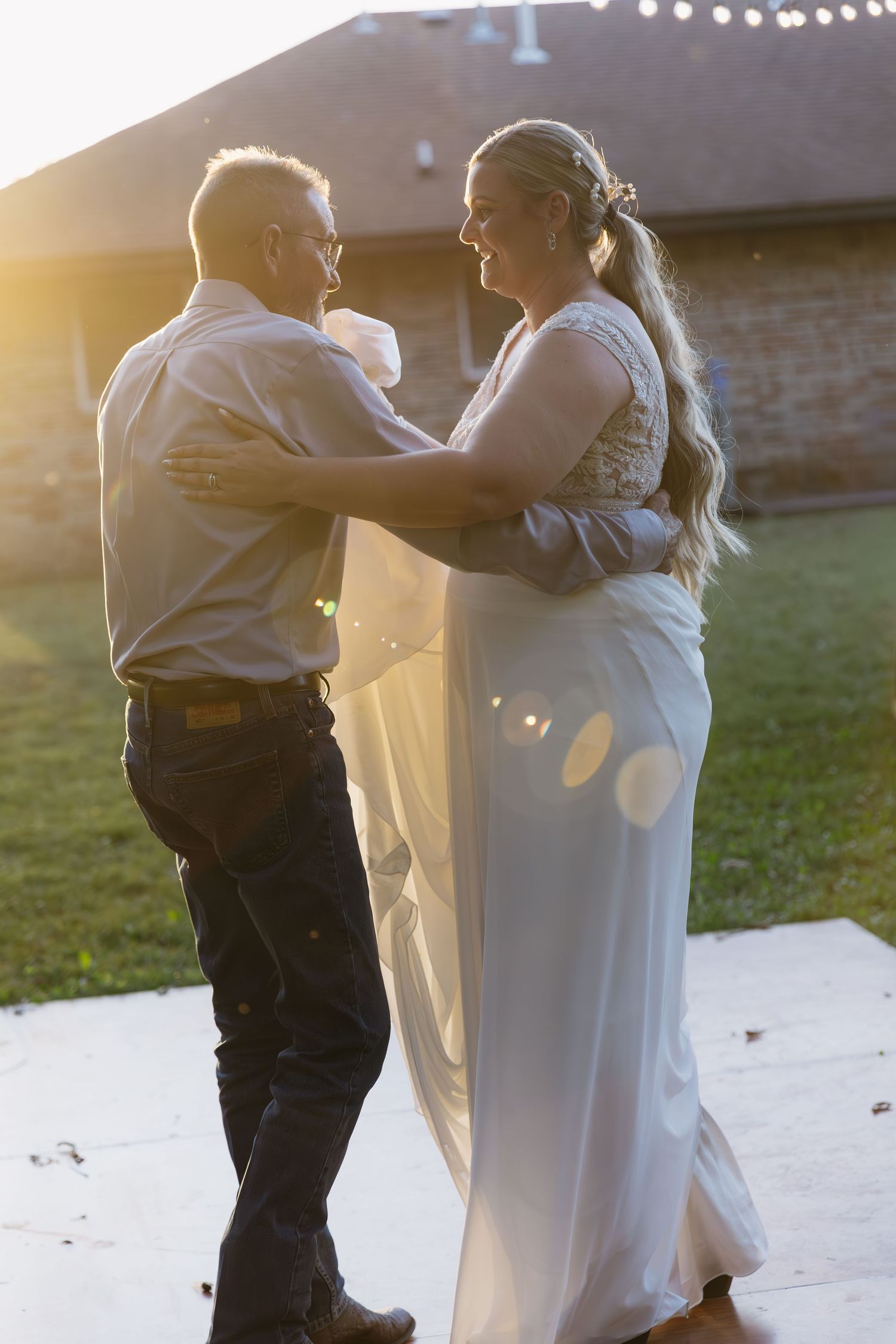 A couple shares a dance together at sunset with string lights glowing in the background.