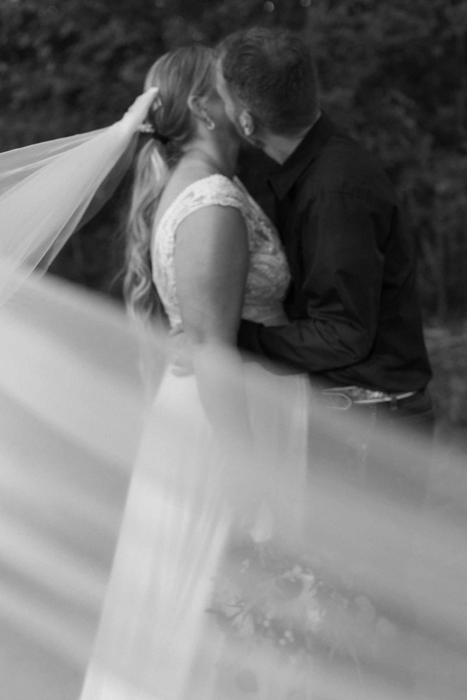 Romantic wedding moment captured through sheer veil outdoors.