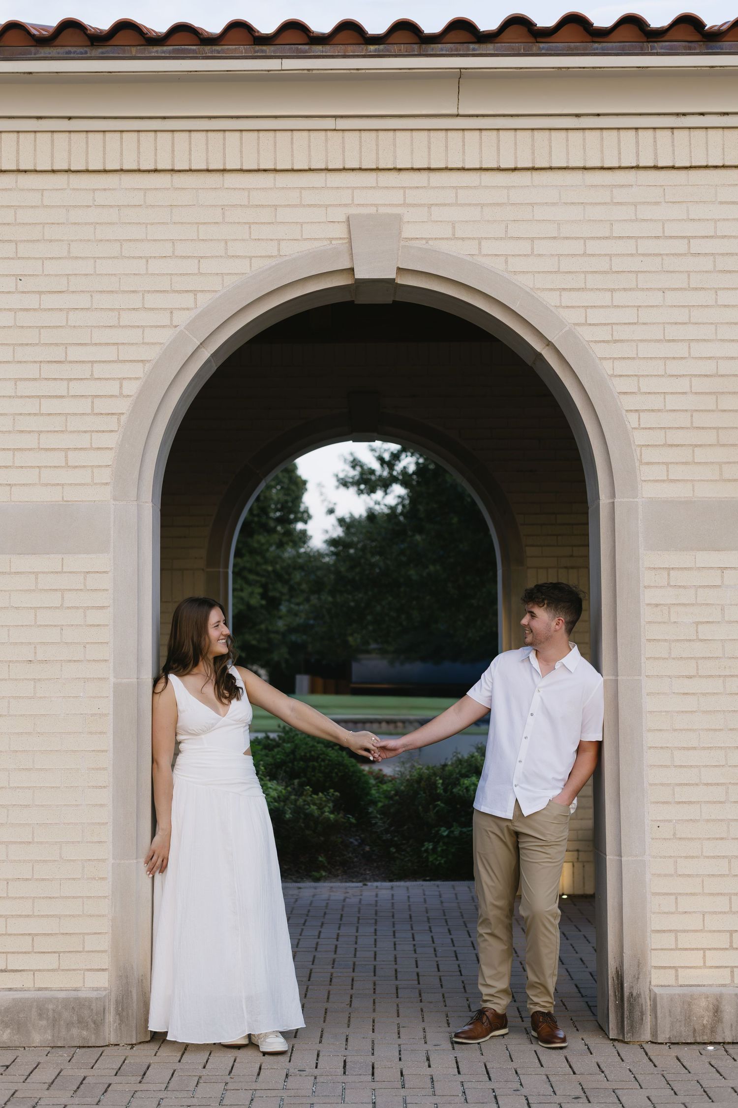 A couple holding hands under a brick archway during an engagement photoshoot.