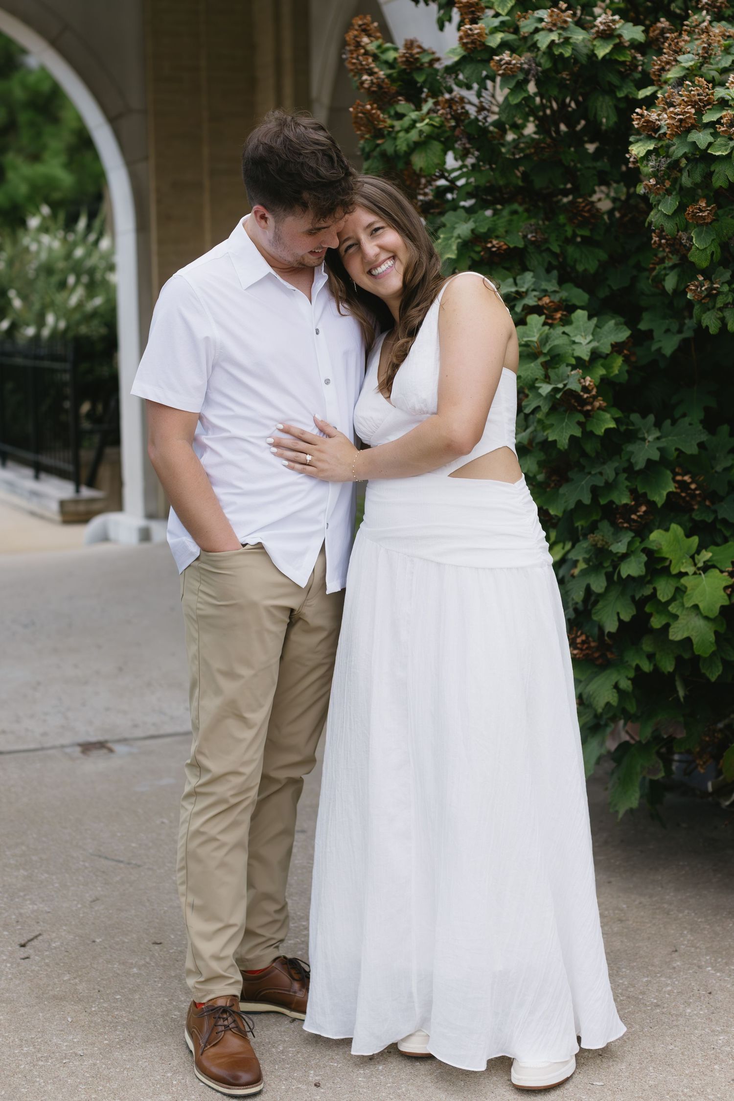 A couple shares romantic moments together near flowering bushes in a garden setting.