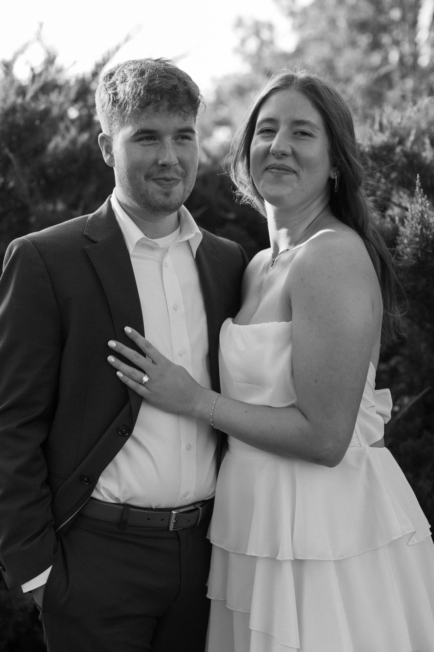 A couple in formal attire shares romantic moments together against an outdoor background in black and white.