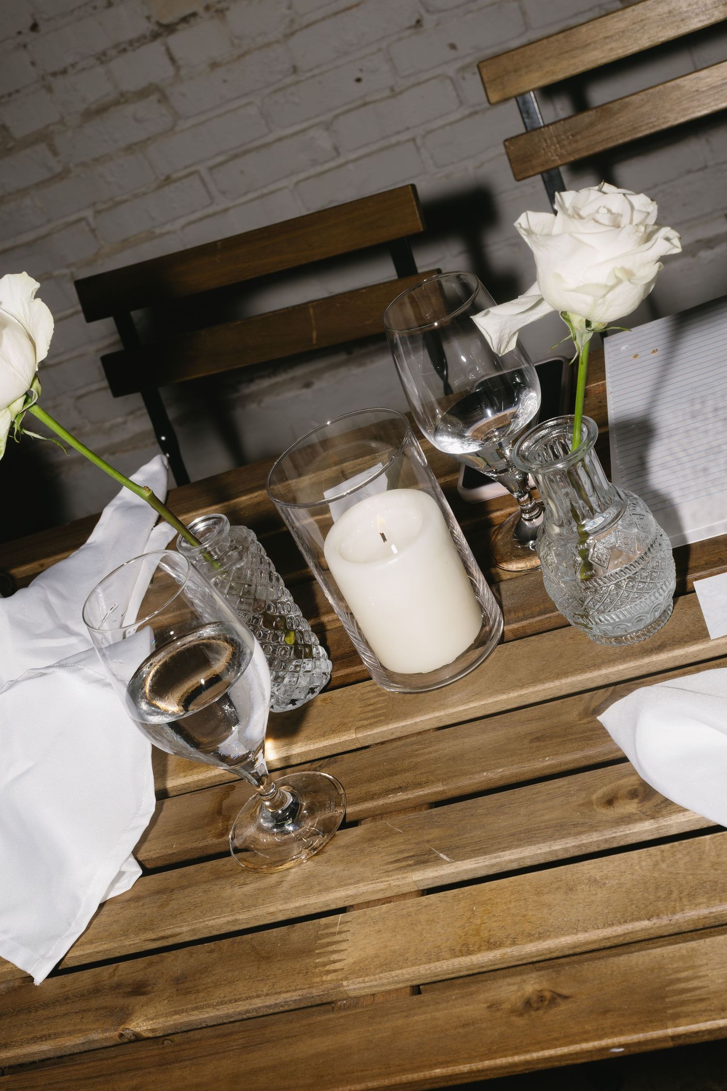 White roses and candles arranged on rustic wooden tables for an elegant event setting.