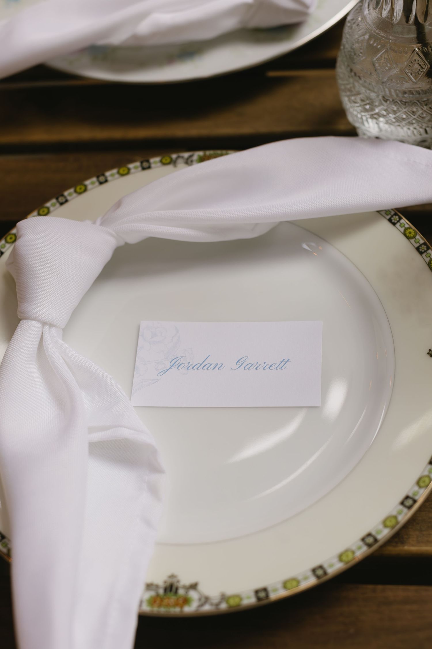 Place settings with white napkins and decorative plates arranged on a wooden table surface for a formal dining event.