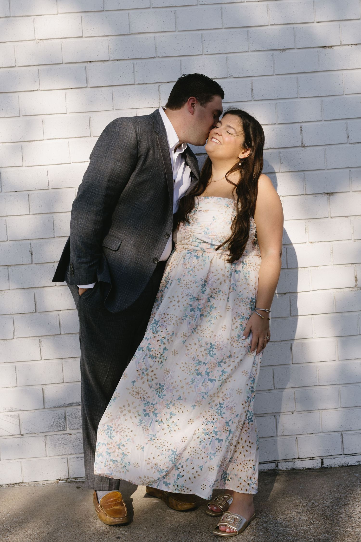 Romantic couple in formal attire poses against white brick wall in a series of playful shots.