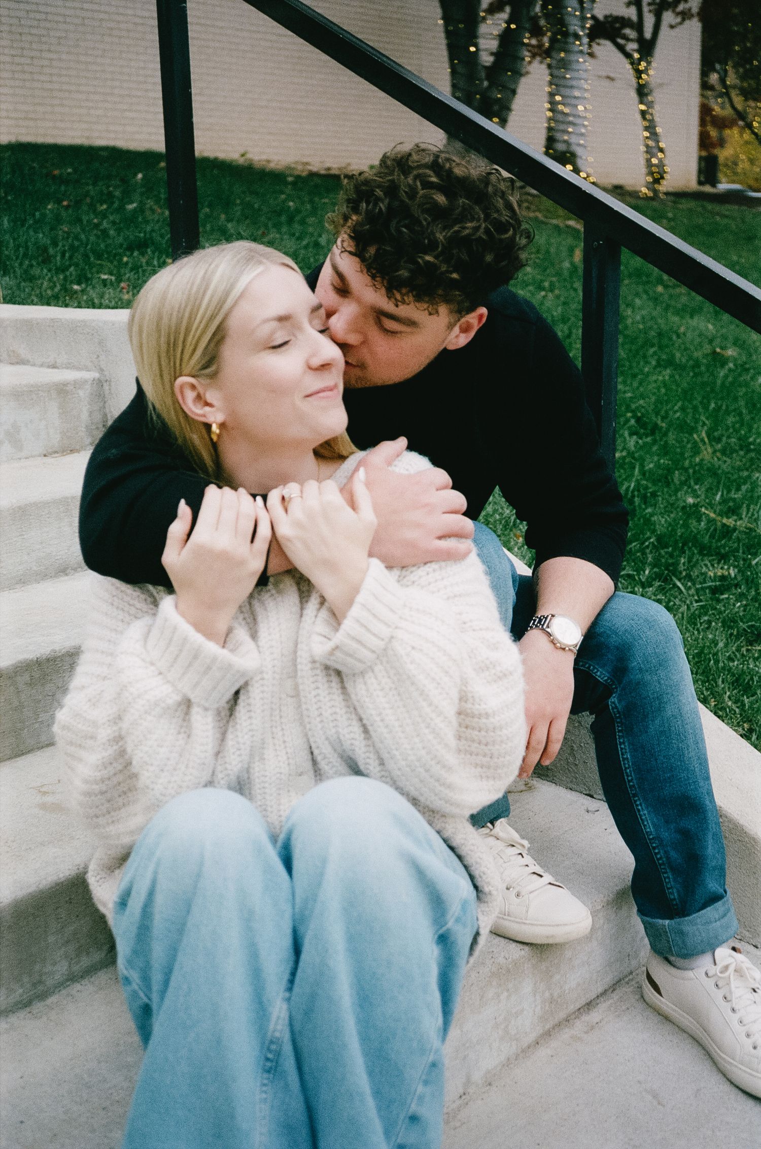 Couple sharing intimate moments while sitting on concrete steps outdoors.