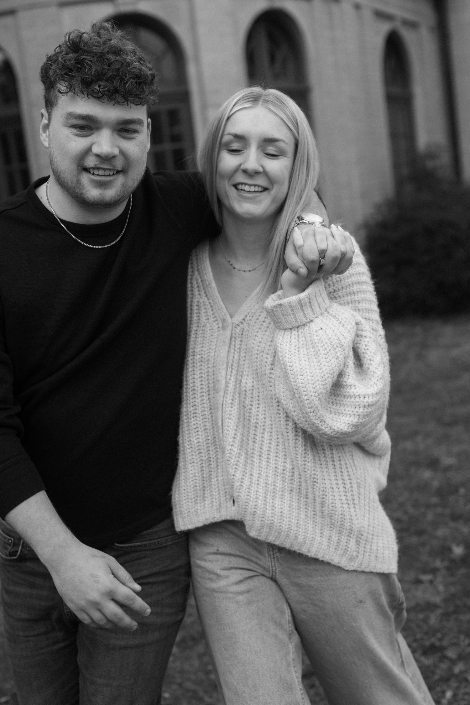 A black and white portrait of a couple in casual attire laughing together outdoors.