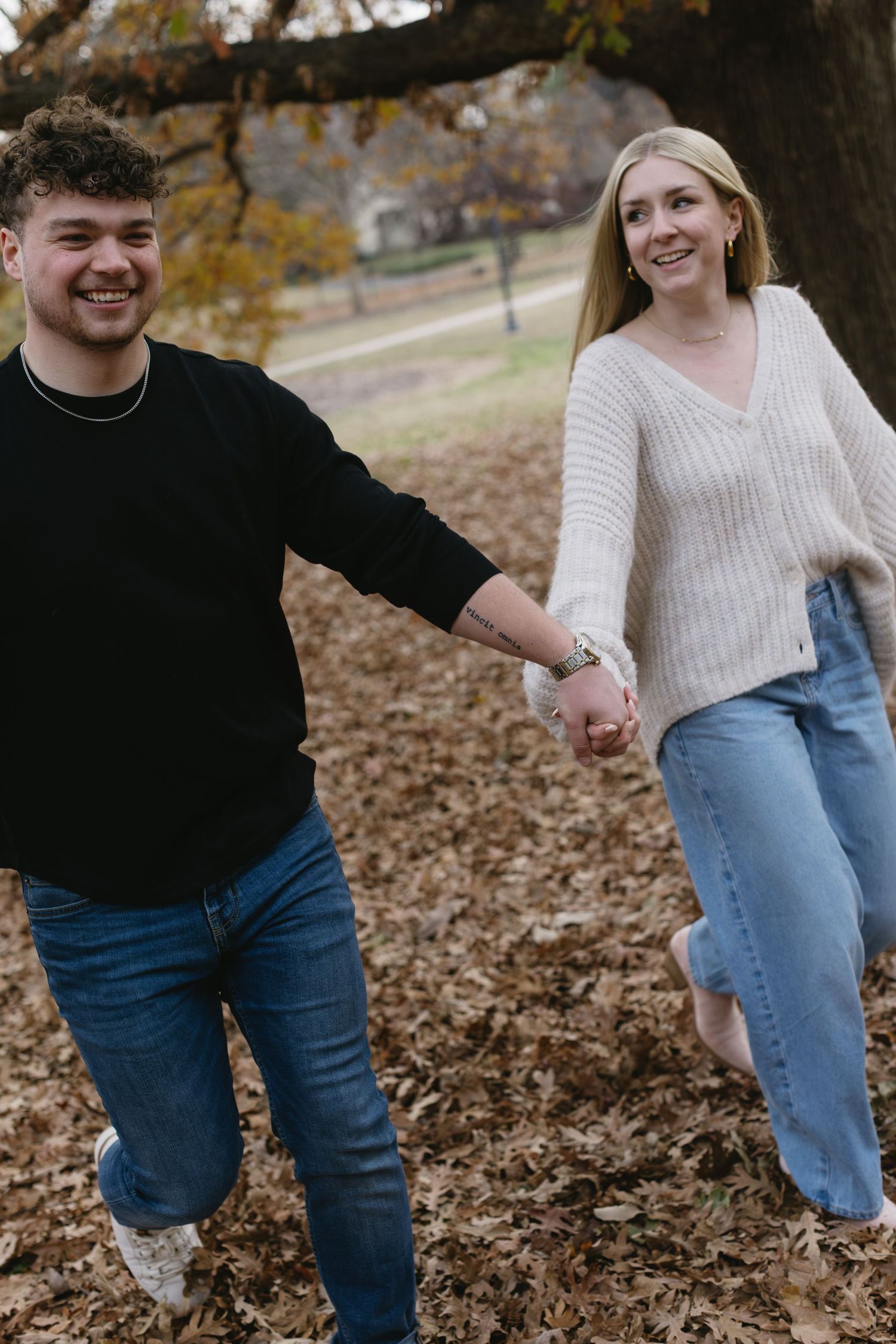 A joyful couple holds hands while walking through fallen leaves on an autumn day.