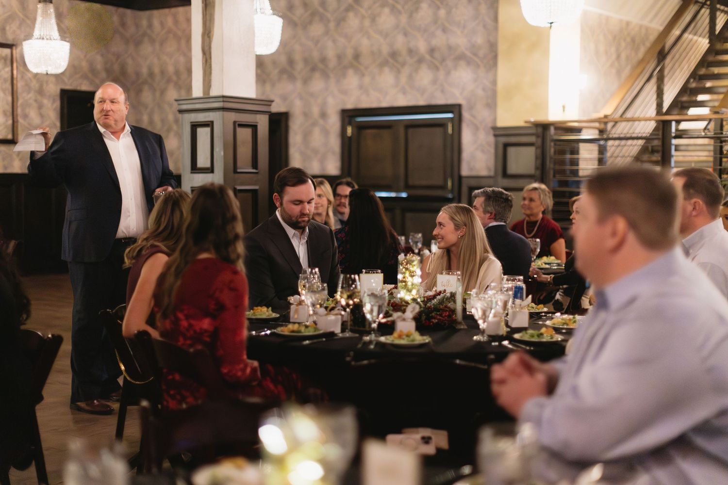 Interior of a dimly lit restaurant dining room with tables and guests during an evening event.
