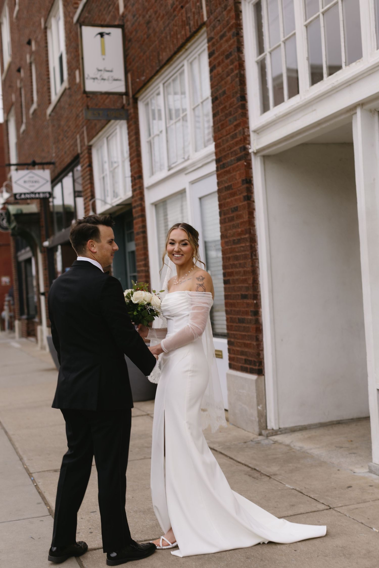 A couple shares a romantic moment on their wedding day outside a brick building with white trim.