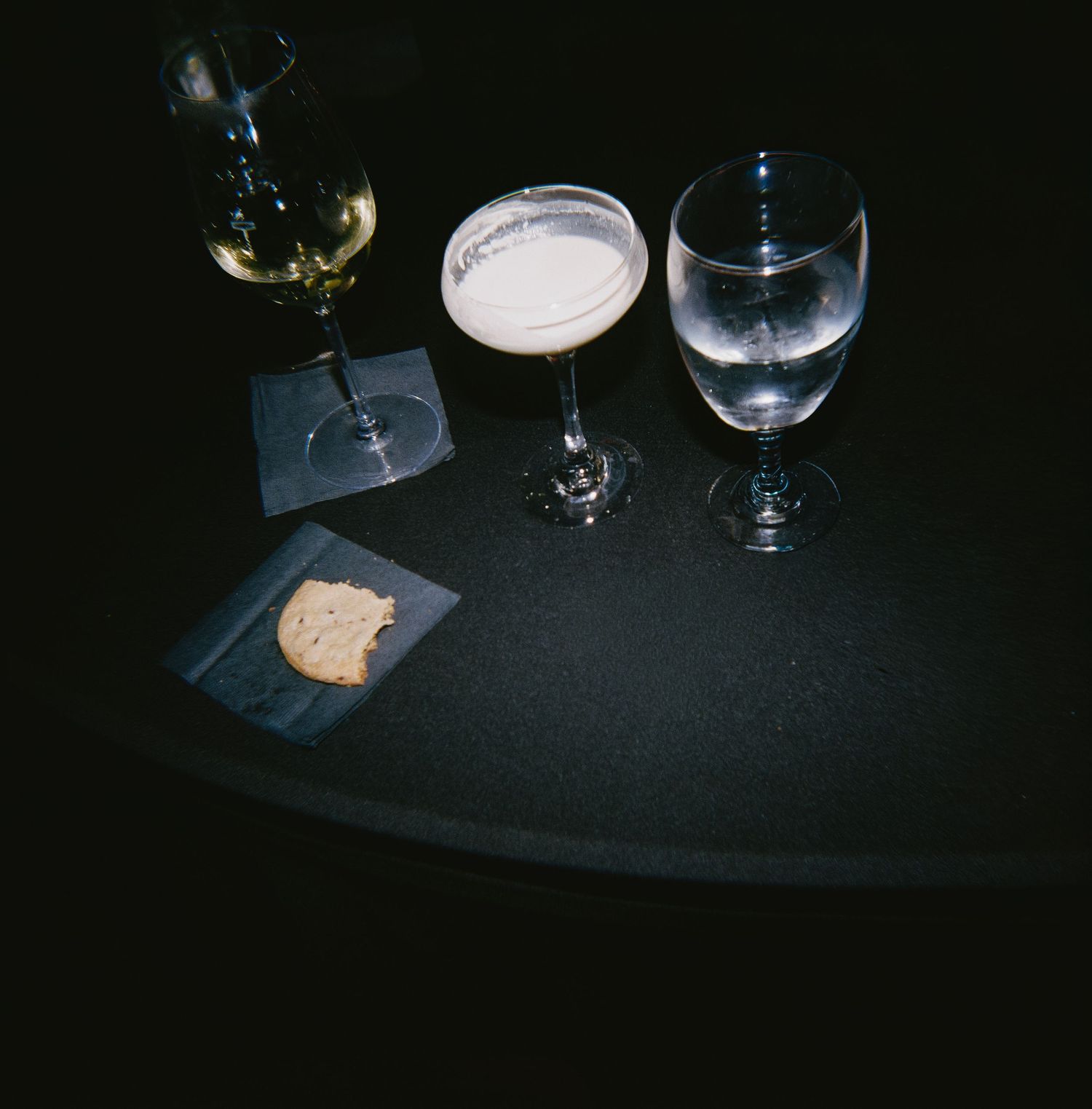 Wine glasses and place settings on a dark tablecloth in dim lighting.
