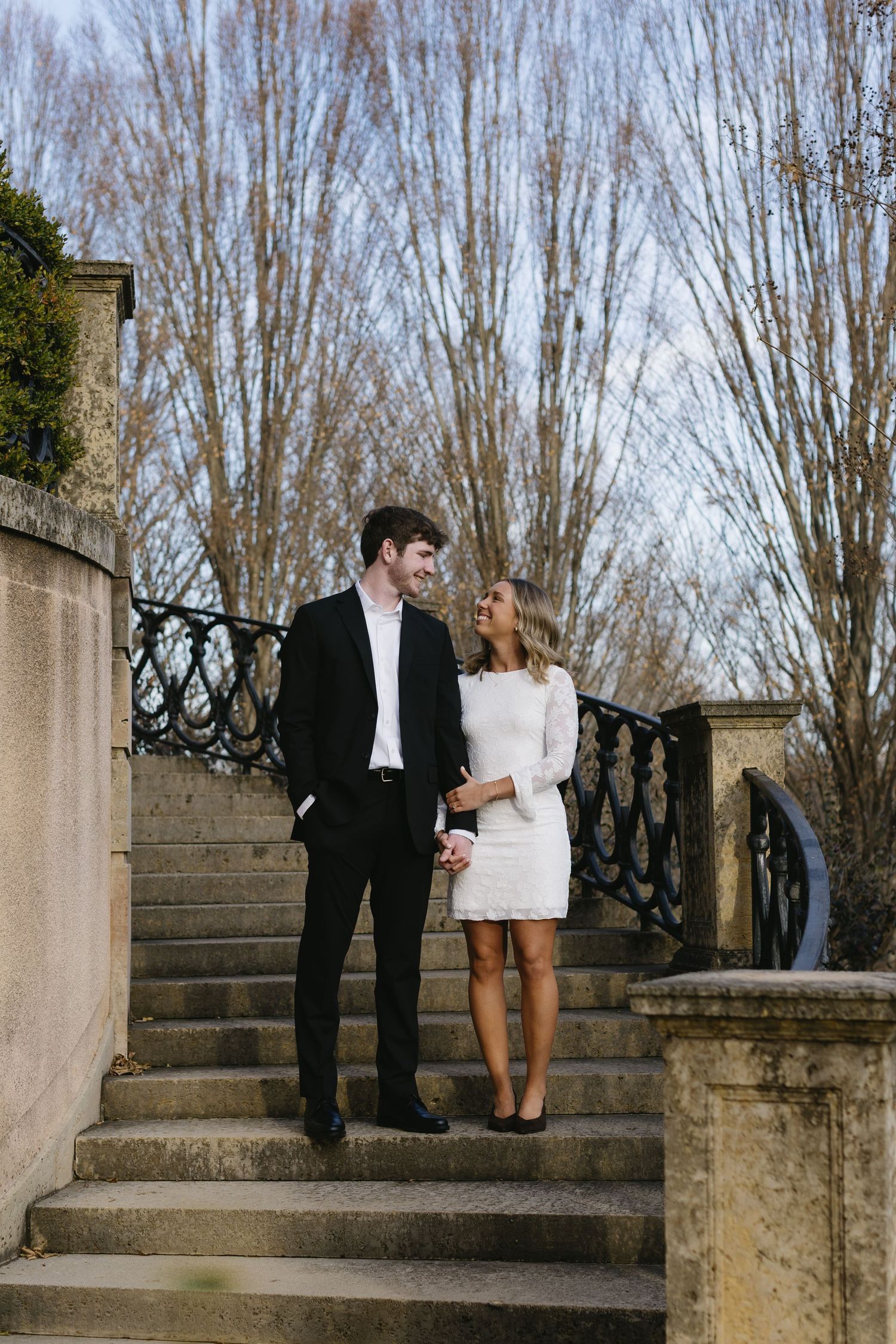 Couple walking down stone steps together in formal attire on a winter day.
