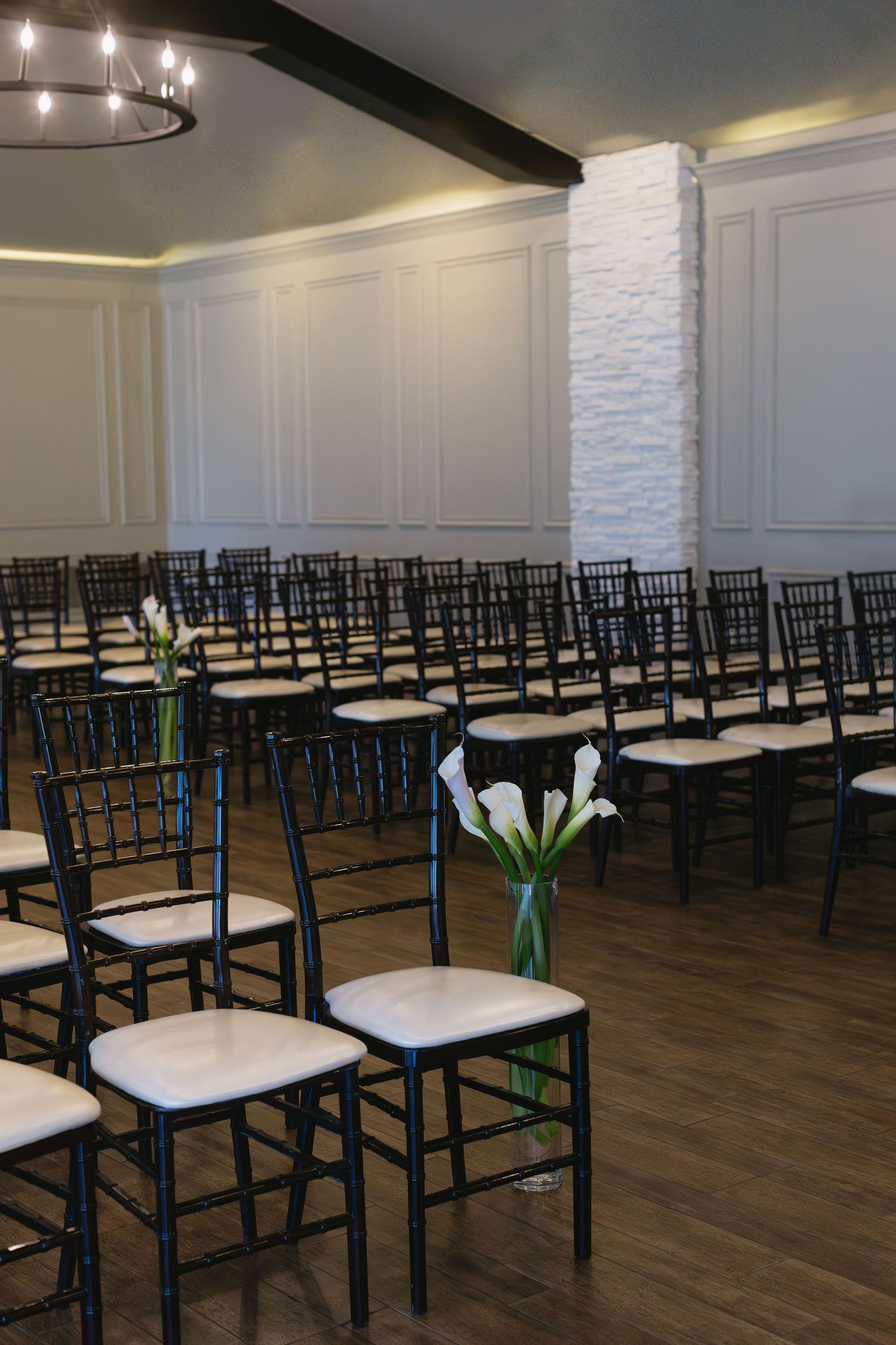 Modern event venue setup with rows of black chairs and white cushions on dark hardwood floors.