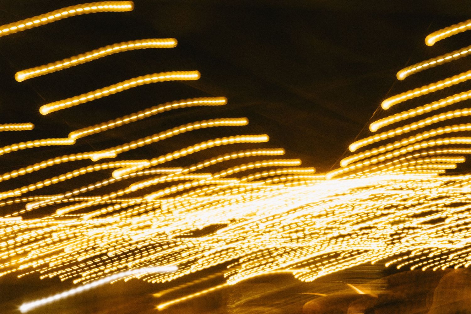 Abstract pattern of golden string lights creating streaks of light against a dark background.