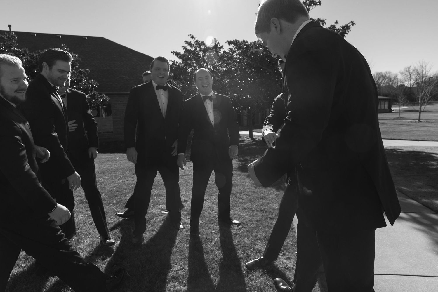 Black and white photo of groomsmen gathered in casual conversation outdoors.
